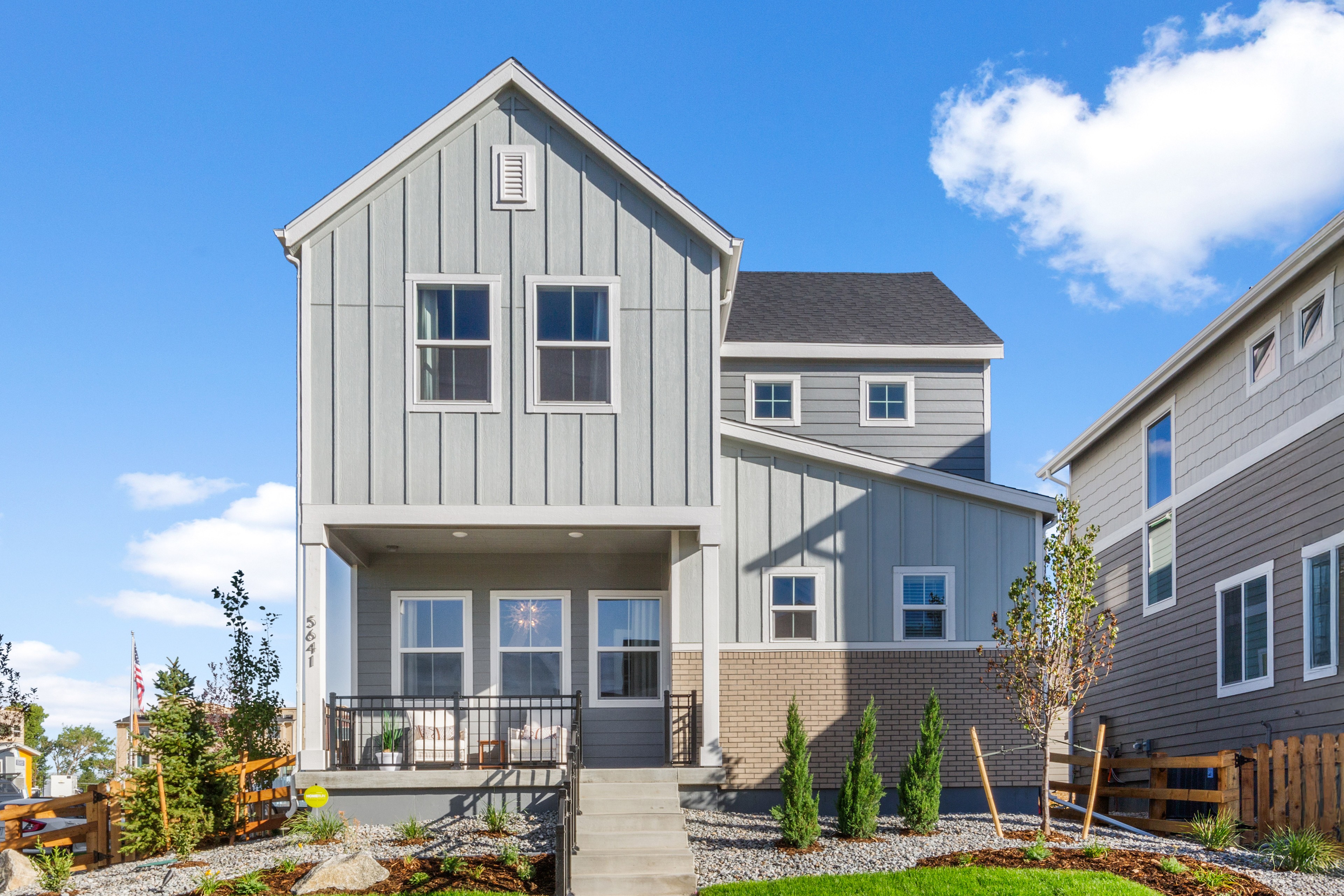 Modern two-story gray house with gable roof, large windows, porch. Dillon Pointe, suburb setting, landscaped yard.