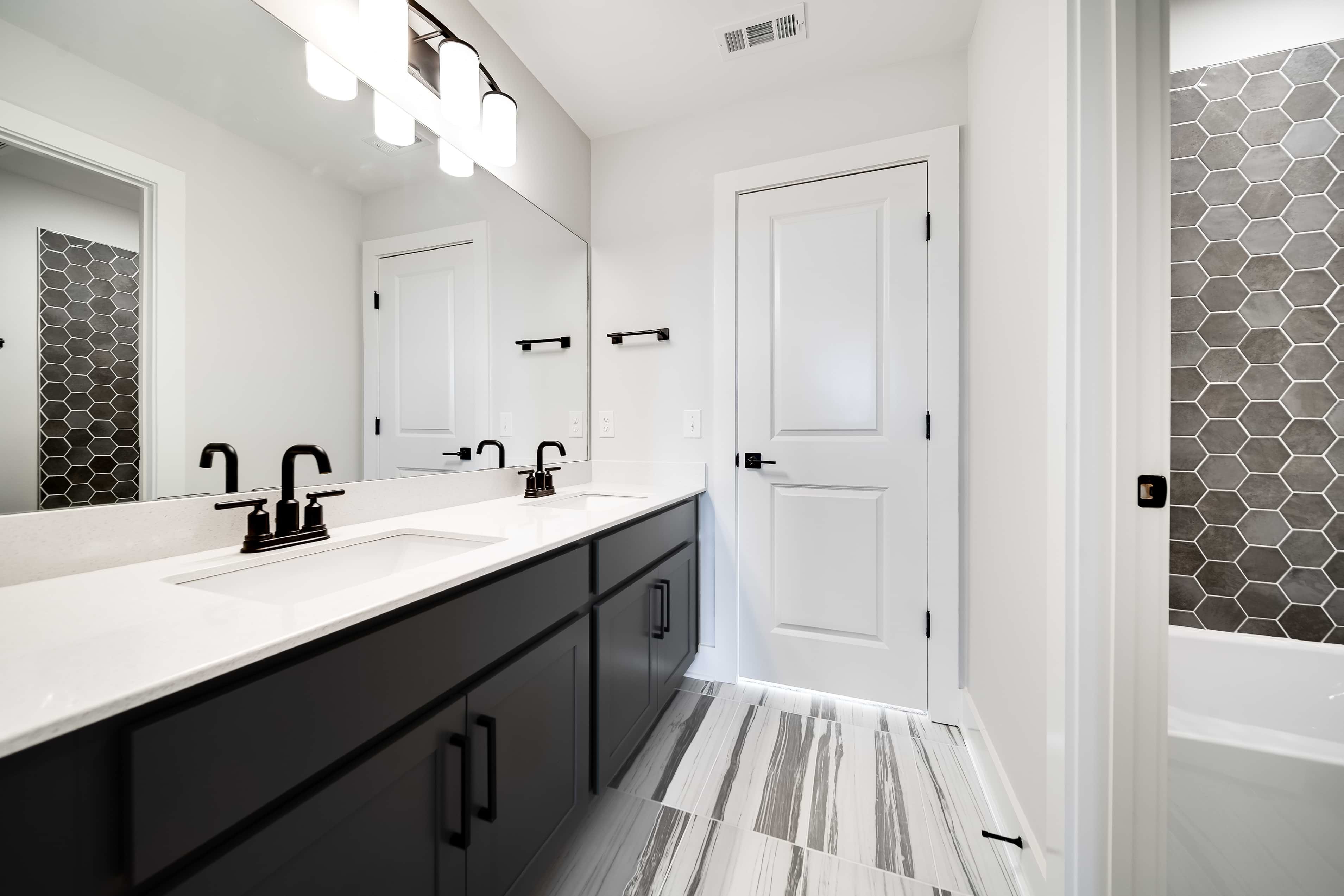 Sleek Dual-Sink Bathroom with Hexagonal Tile in Richvale Estates Modern bathroom with dual sinks, black fixtures, hexagonal tile wall, chic Richvale Estates setting.