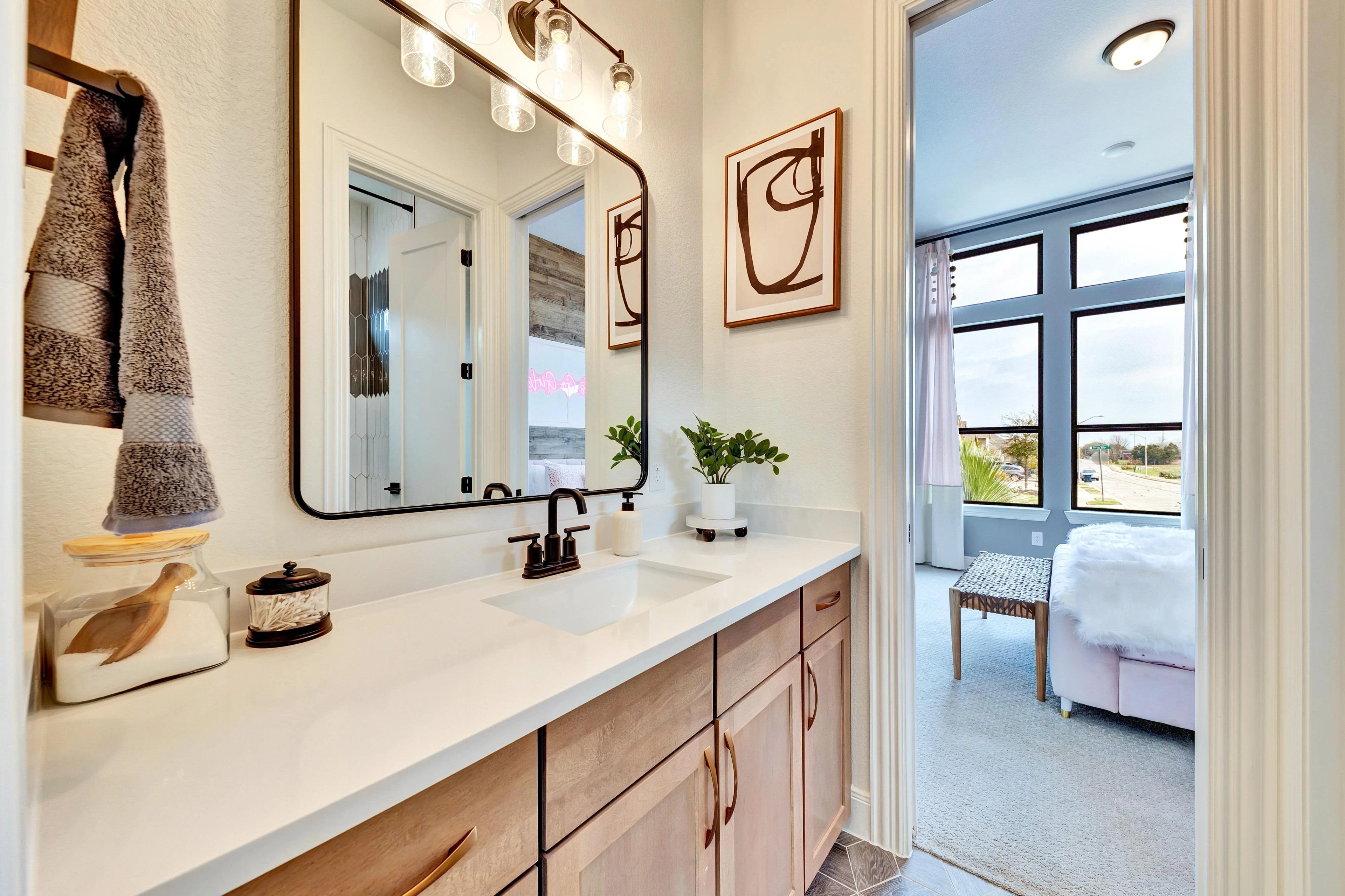 Elegant Bathroom Vanity at Hawkes Landing with Modern Design Modern bathroom vanity with wood cabinets, large mirror, and black fixtures in Hawkes Landing. Window to bright room.