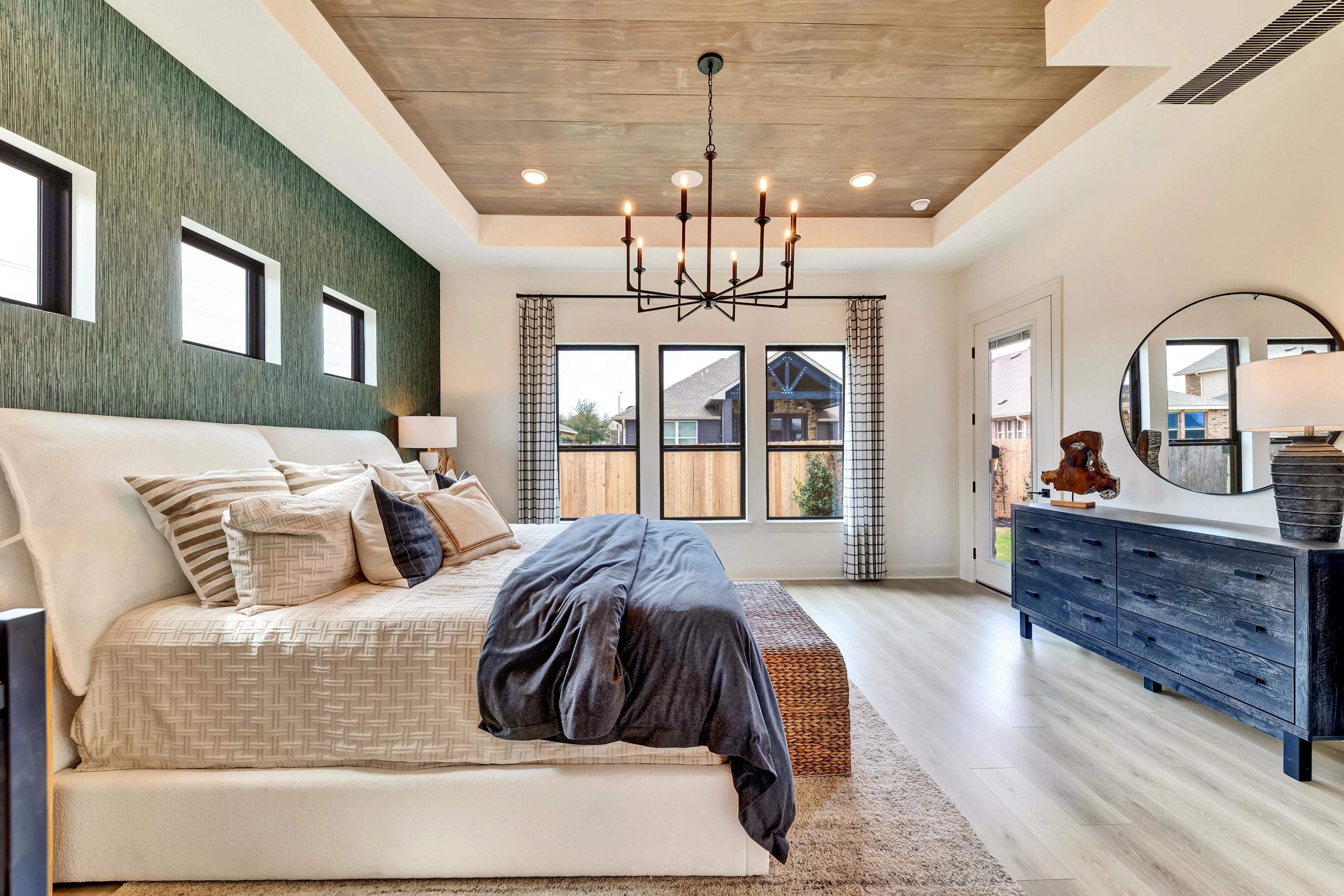Elegant Bedroom with Modern Chandelier in Hawkes Landing, Texas Luxurious bedroom with light wood flooring, green accent wall, modern chandelier, large windows. Hawkes Landing, Texas.