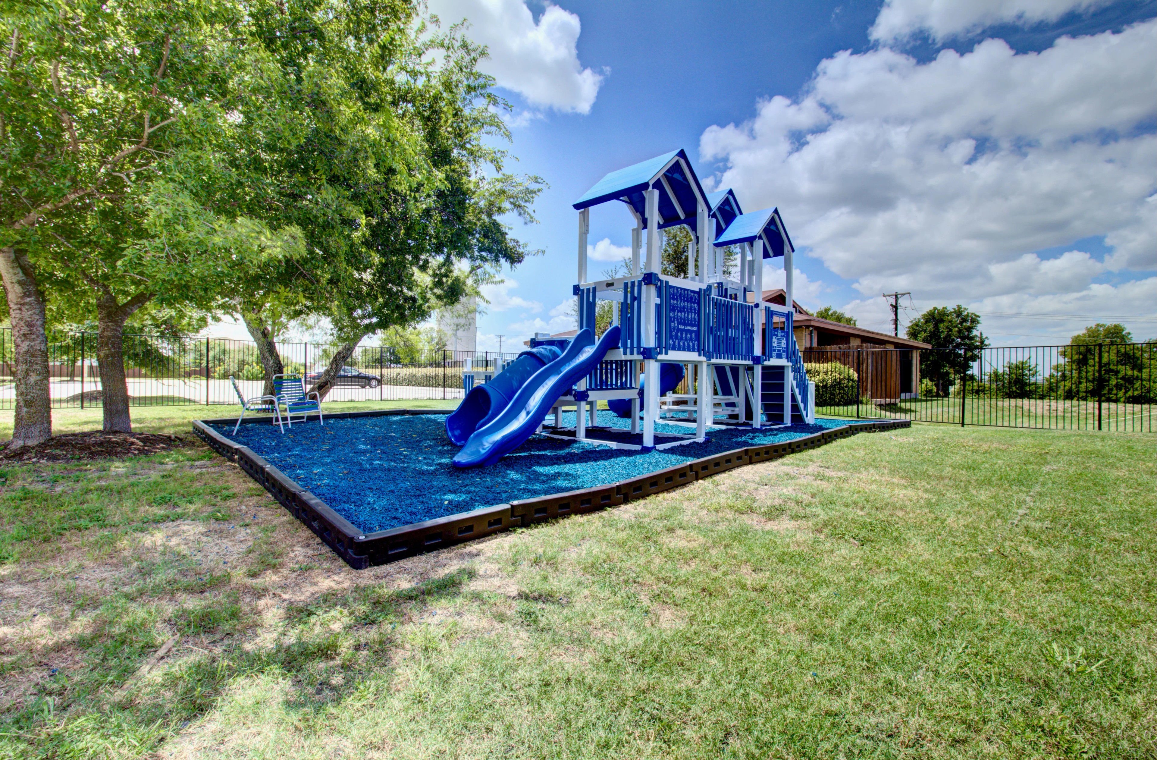Blue Playground in Cloud Country Residential Community Blue and white playground with slides in a grassy area, surrounded by trees and a fence, located in a sunny residential community.