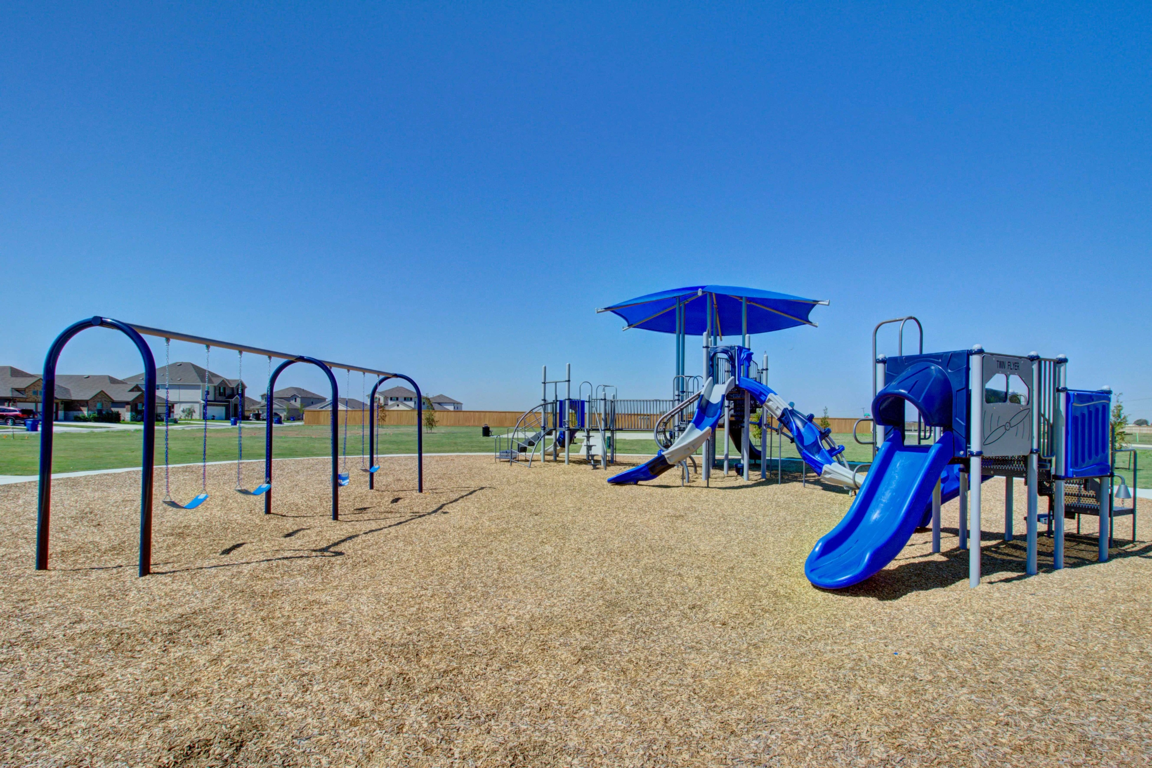 Playground at Dauer Ranch Community Featuring Swings and Slides Playground with swings, slides, and canopy in Dauer Ranch community park, set against suburban homes and blue sky.