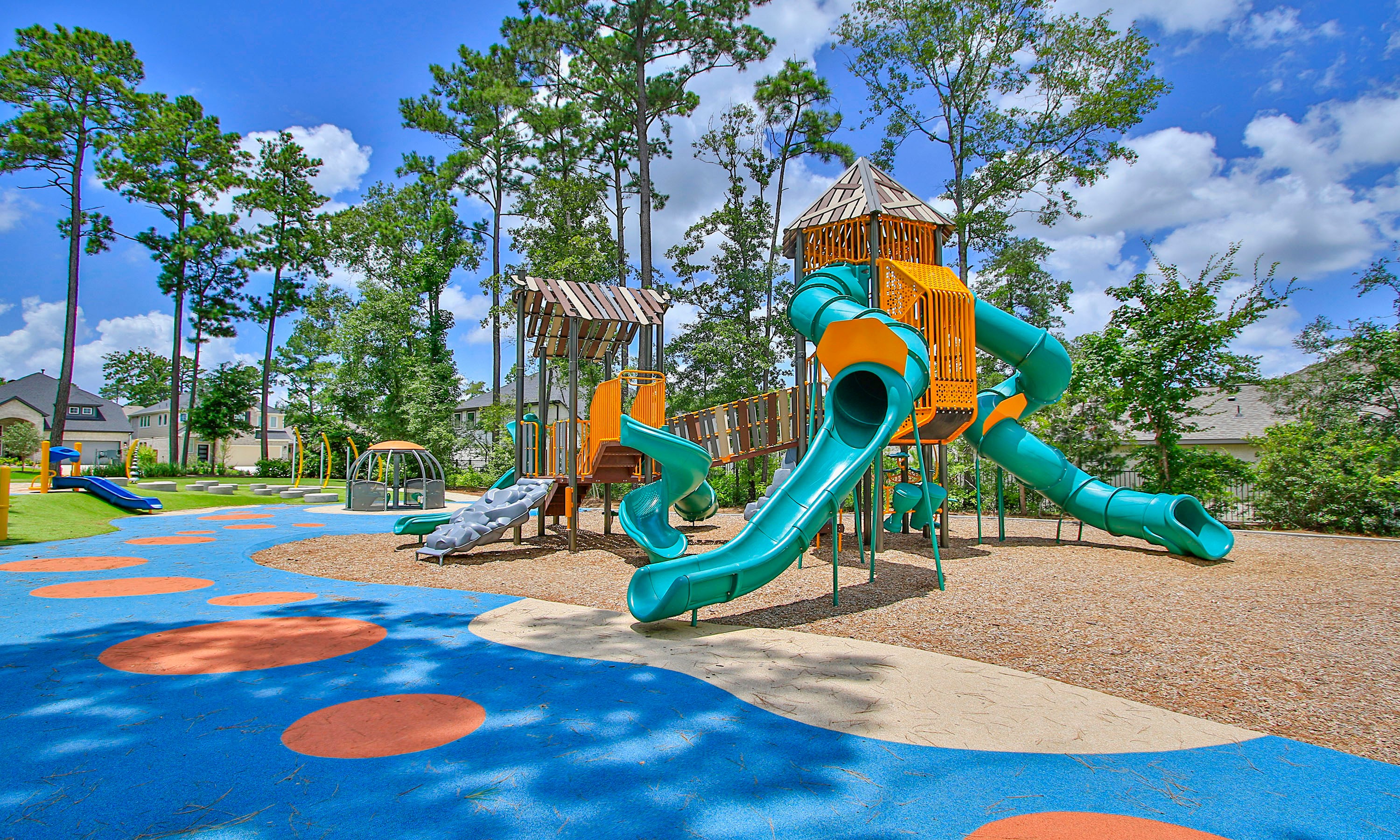 The Woodlands Hills Playground with Colorful Slides and Towers Colorful playground with slides and towers in The Woodlands Hills, surrounded by trees and homes.
