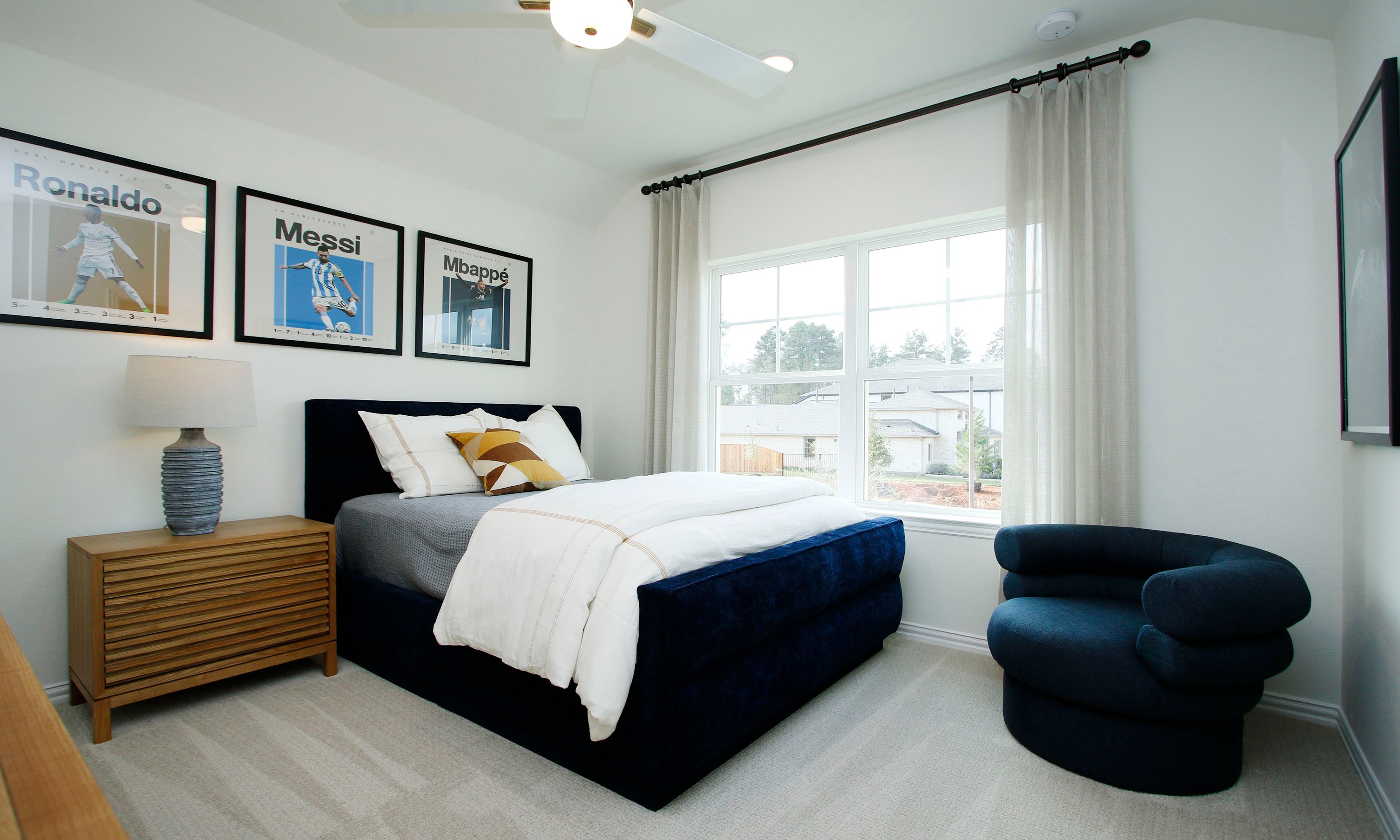 Luxurious Bedroom Design in The Woodlands Hills with Modern Art Elegant bedroom in The Woodlands Hills with plush navy bed, modern art, and large window offering serene views.