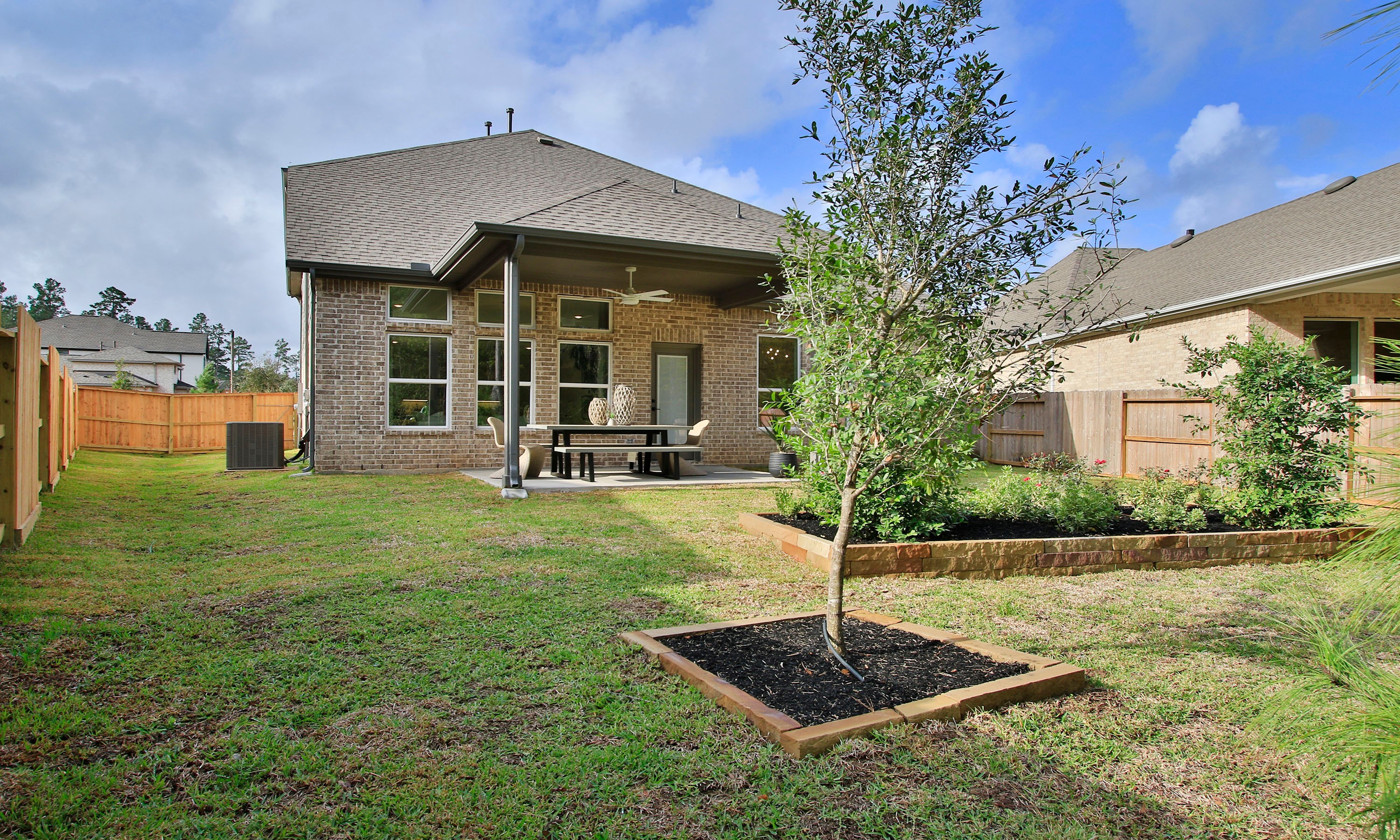 Modern Brick House Patio in The Woodlands Hills Community Backyard with brick house, covered patio, ceiling fan, lush garden in The Woodlands Hills community.