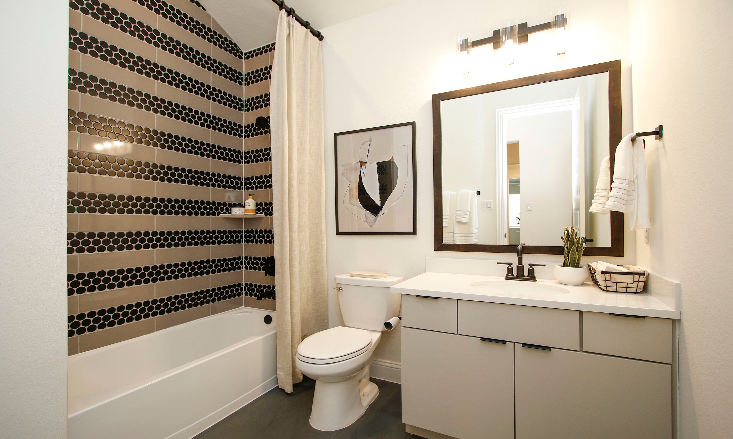 Luxurious Bathroom Design in The Woodlands Hills Community Elegant bathroom with black hexagon tile, vanity, framed mirror, and art in The Woodlands Hills community.