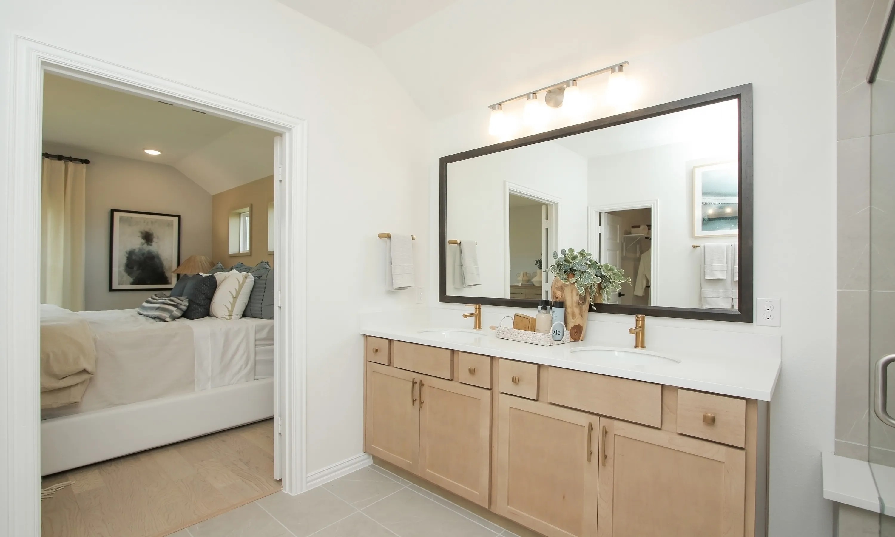 Ellis Cove Elegant Bathroom with Double Vanity and Gold Fixtures Modern bathroom with double vanity, large mirror, and gold fixtures. Overlooks elegant bedroom in Ellis Cove community.