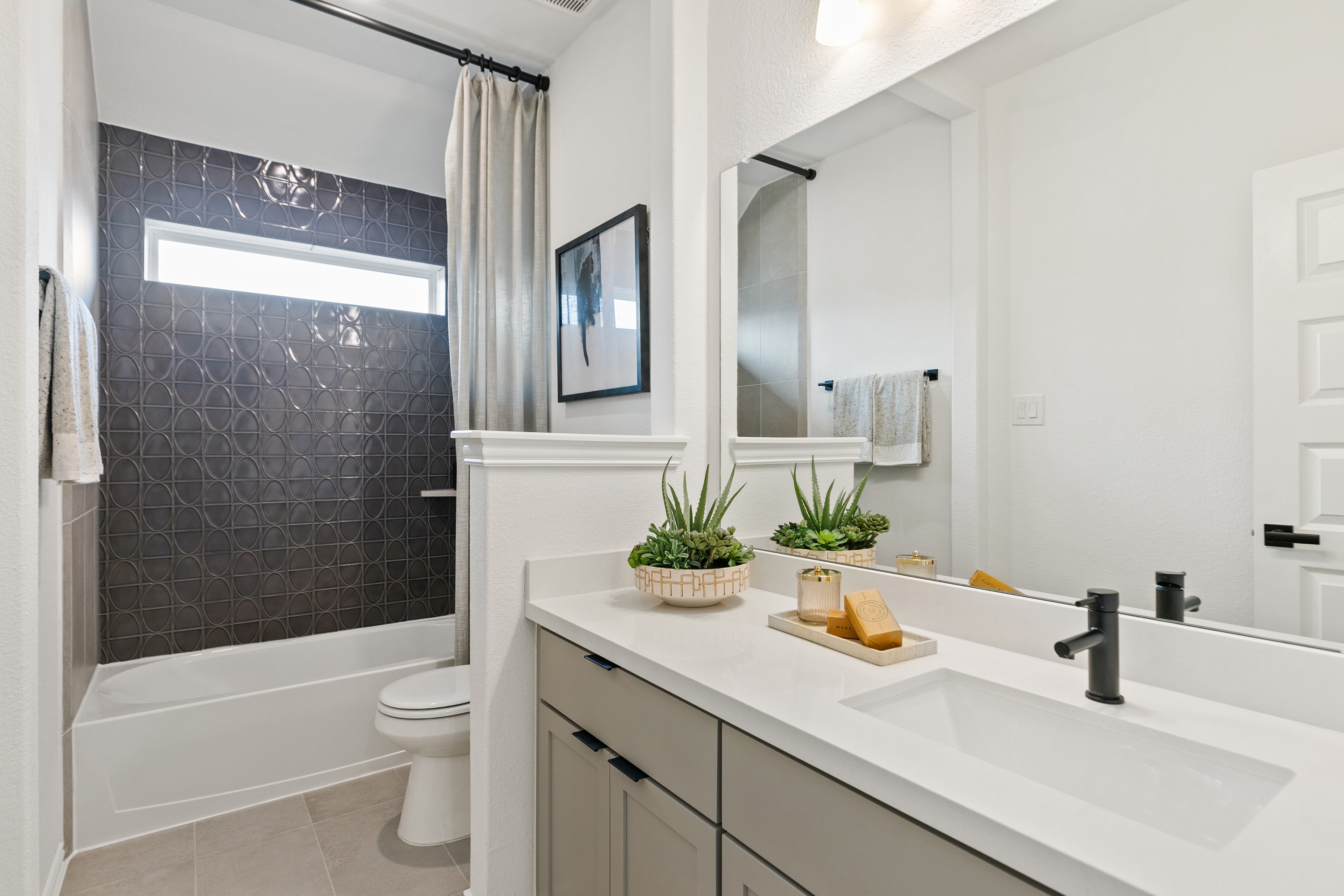Elegant Modern Bathroom with Geometric Tile in Park at Eldridge Modern bathroom with geometric dark tile, wide mirror, sleek faucet, and succulent decor in Park at Eldridge.