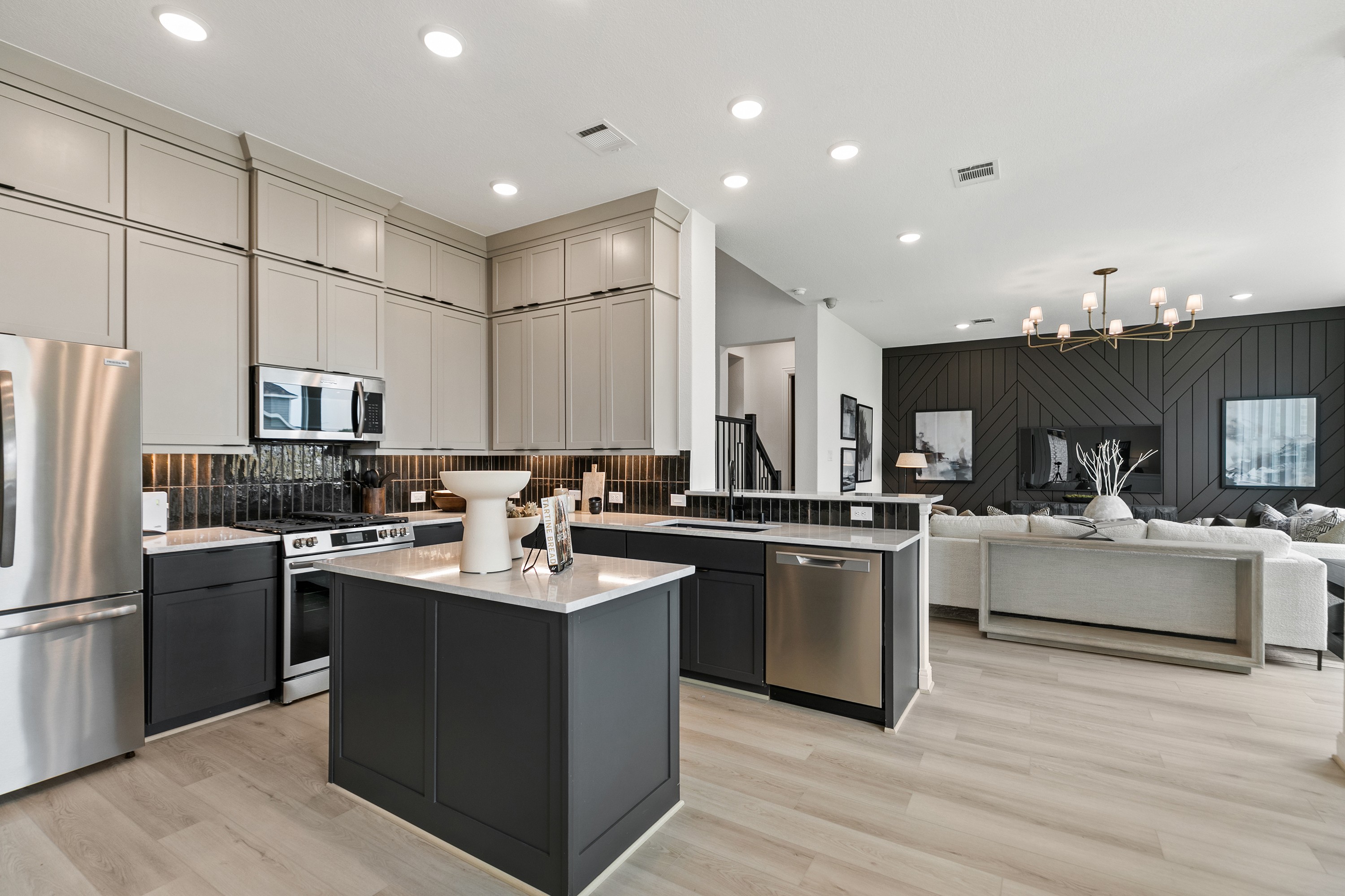 Modern Kitchen and Living Room at Park at Eldridge, Texas Modern kitchen with island, stainless appliances, open living room, wood accent wall, Park at Eldridge, Texas.
