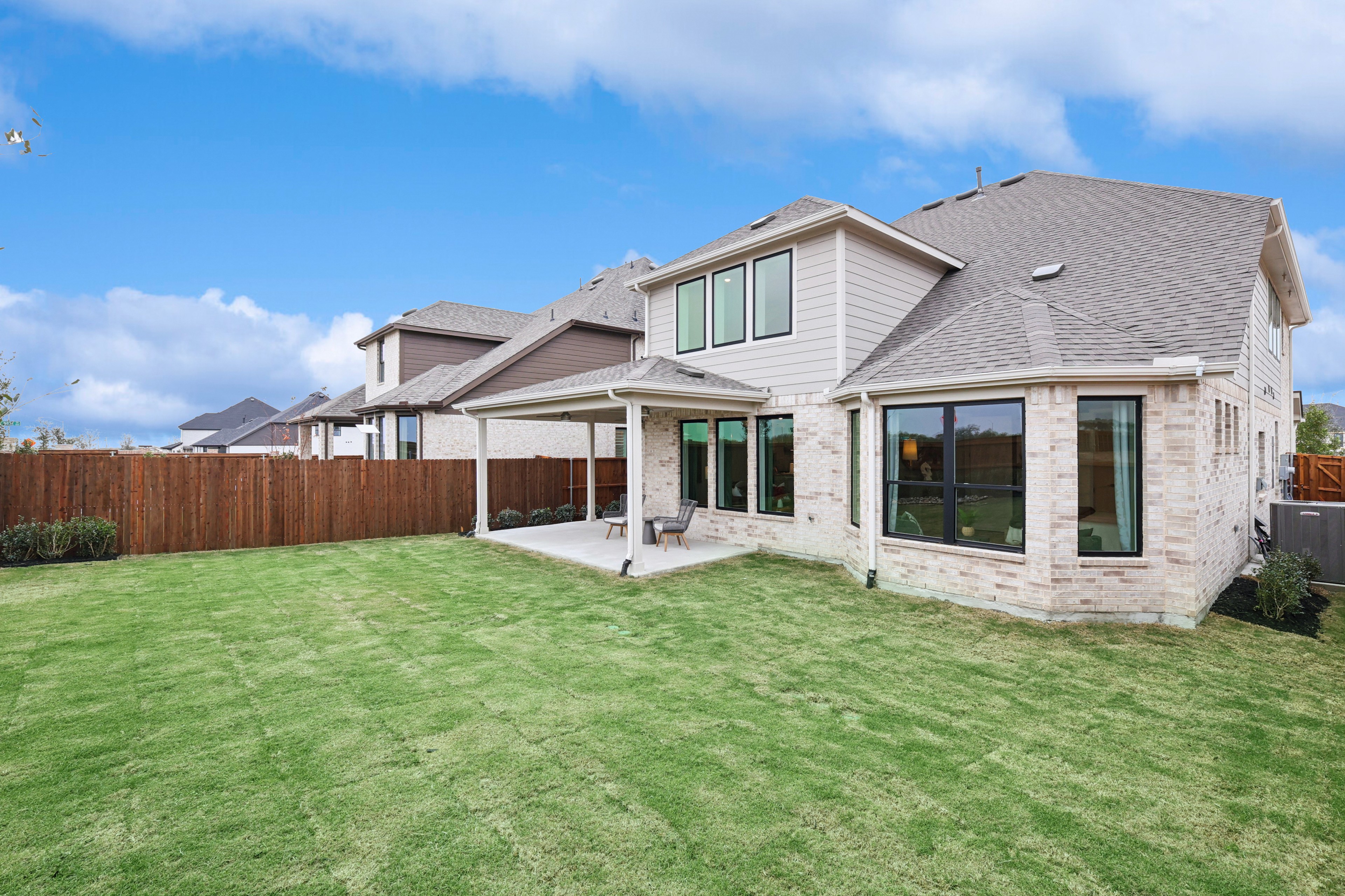 Wildflower Ranch Home with Expansive Backyard and Patio Spacious backyard with covered patio, brick exterior, and manicured lawn in Wildflower Ranch community.