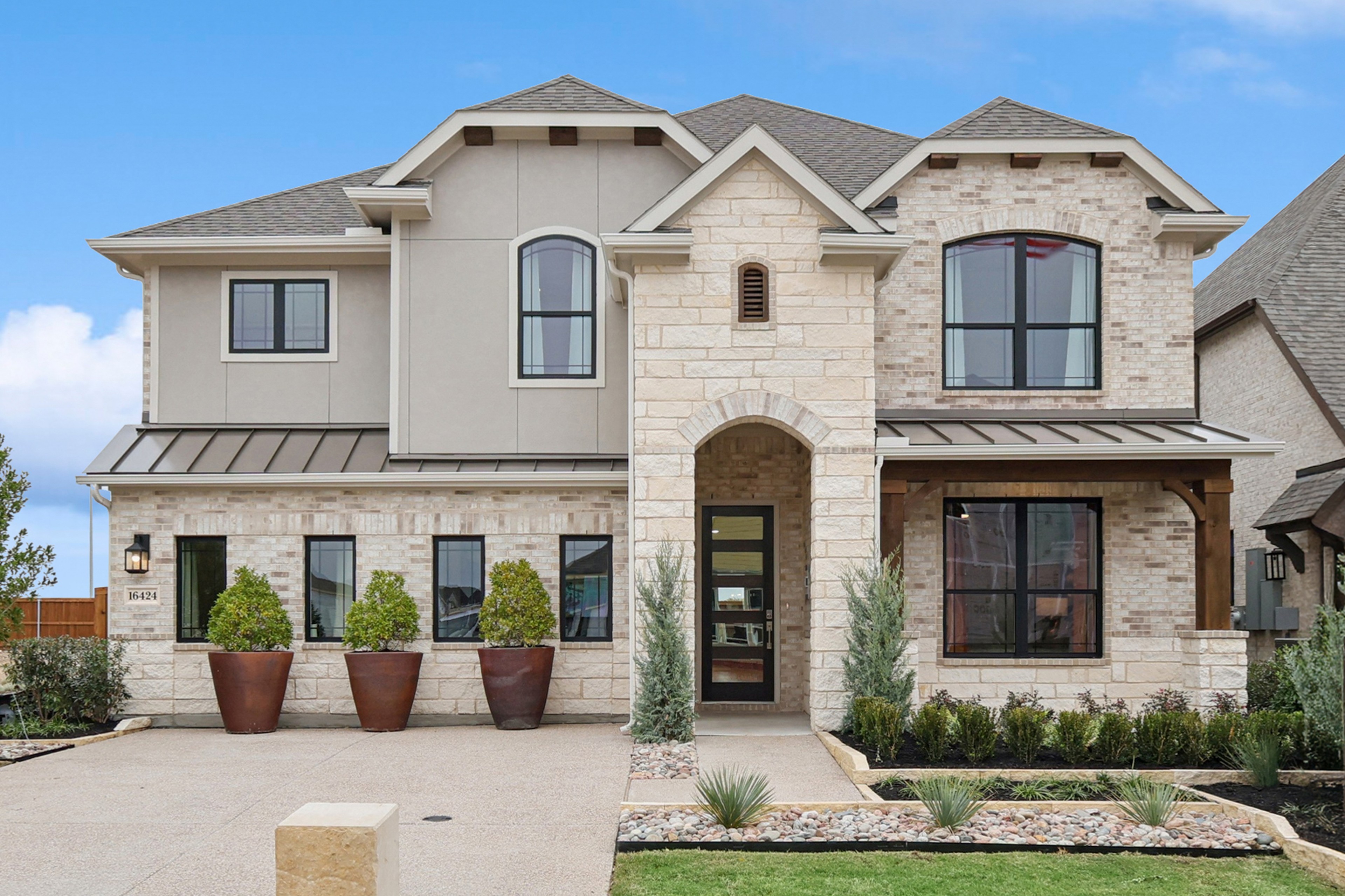 Two-Story Stone and Brick Home at Wildflower Ranch Two-story stone and brick house with arched entry, large windows, modern landscaping, Wildflower Ranch.