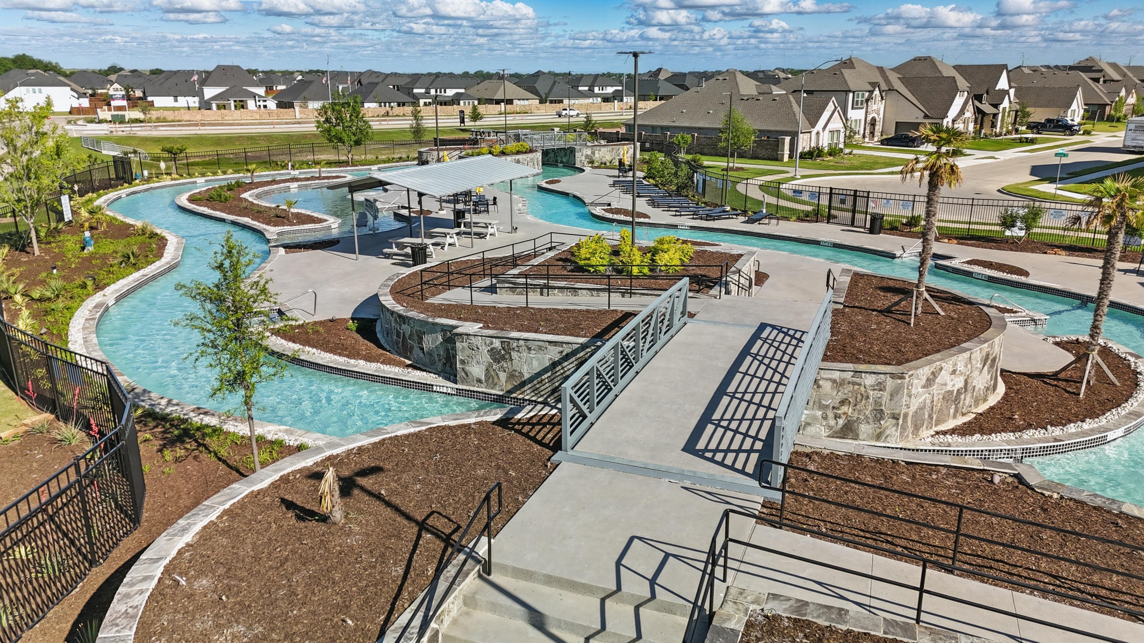 Lazy River and Modern Homes at Wildflower Ranch, Texas Lazy river at Wildflower Ranch community, Texas. Features stone walls, bridges, lush landscaping, and modern homes.