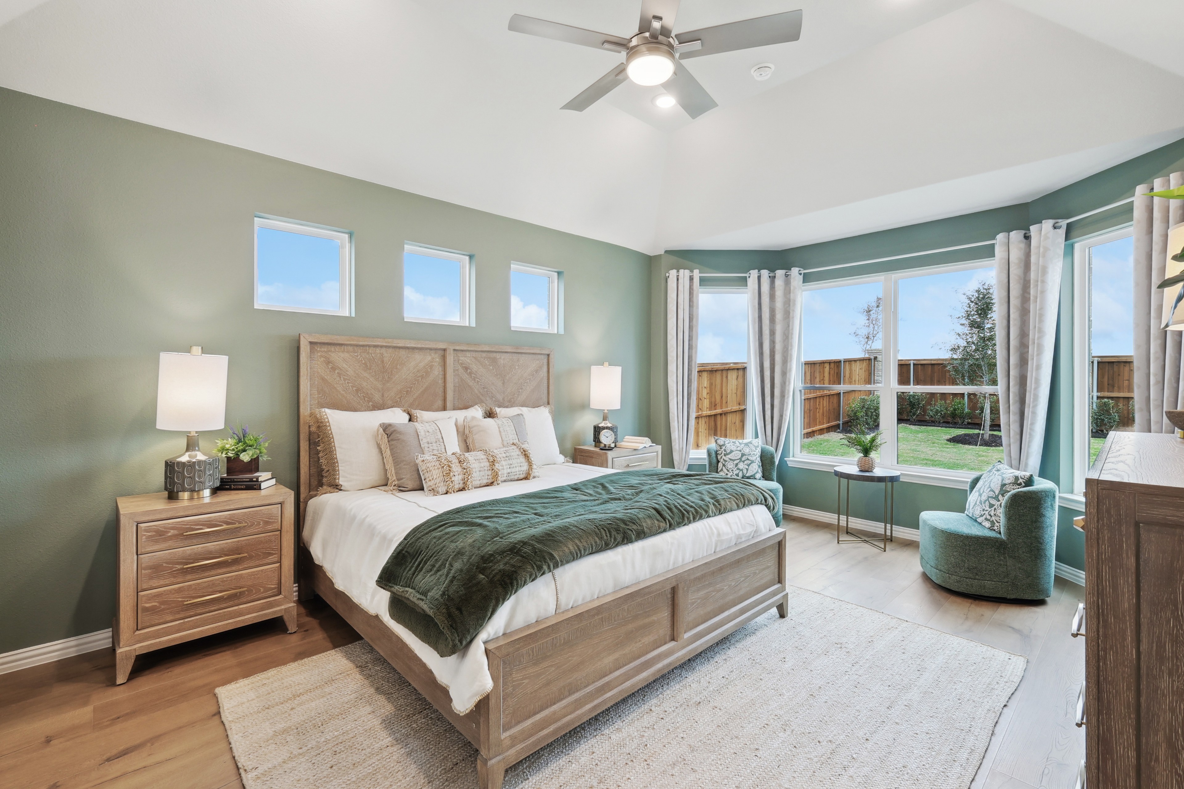 Elegant Bedroom Design at Wildflower Ranch Highlighting Green Accents Spacious bedroom with green accent wall, large windows, ceiling fan, wood furniture in Wildflower Ranch.
