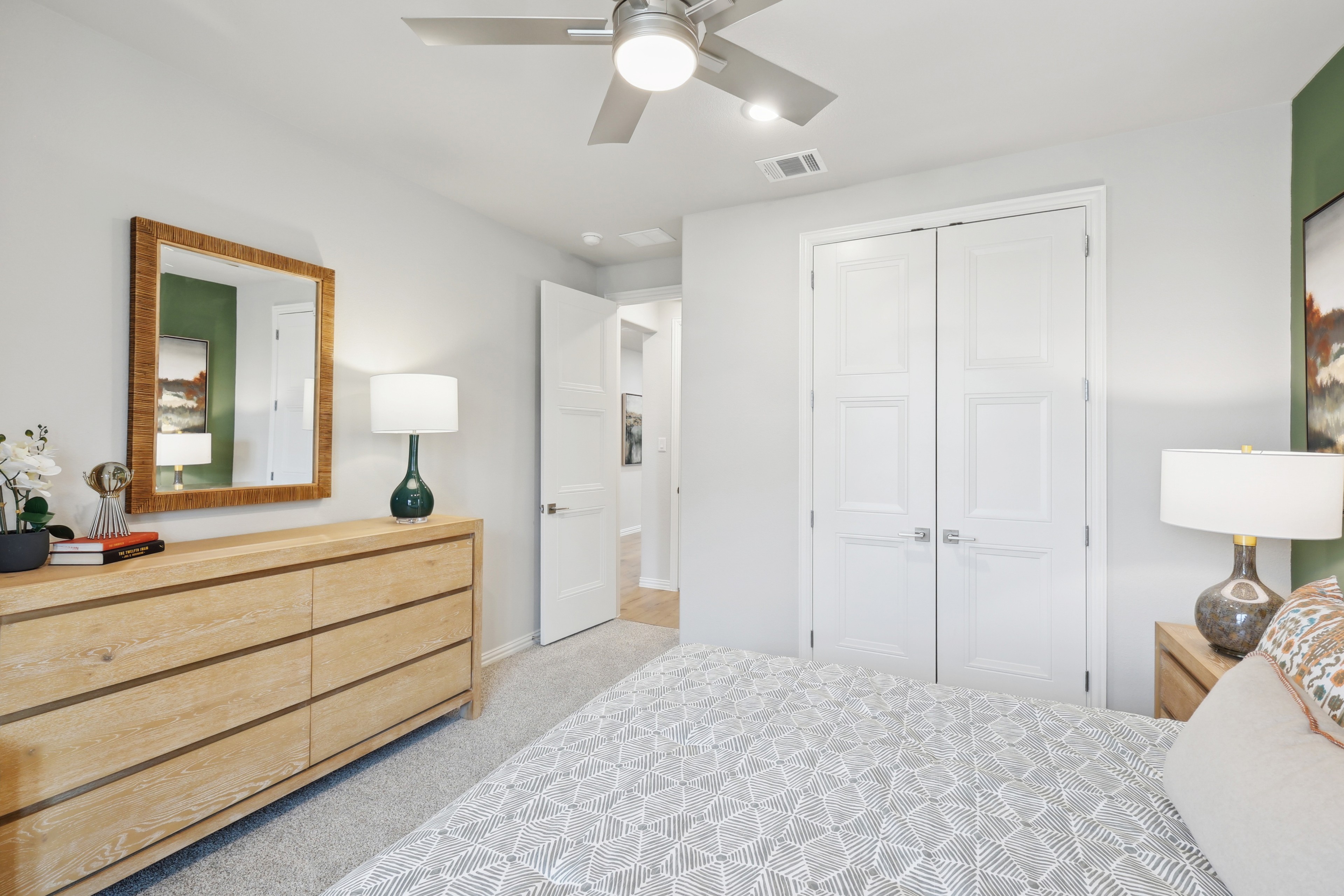 Modern Bedroom with Wood Dresser and Ceiling Fan at Wildflower Ranch Modern bedroom, wood dresser, mirror, ceiling fan, green accent wall, Wildflower Ranch, light-filled, door.