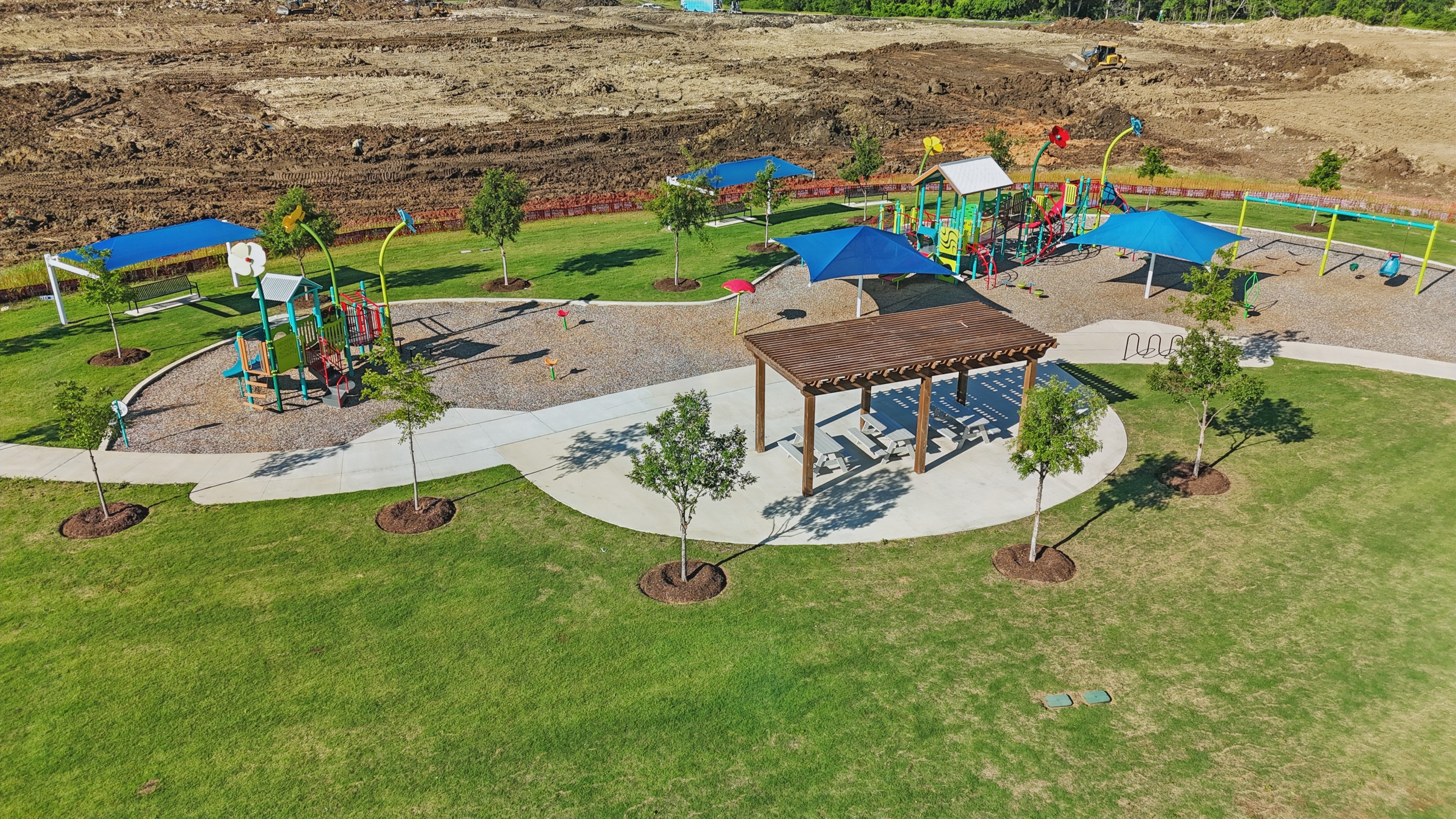 Wildflower Ranch Playground with Shaded Areas and Lawn Playground in Wildflower Ranch with colorful structures, shaded tables, green lawn, and construction in the background.