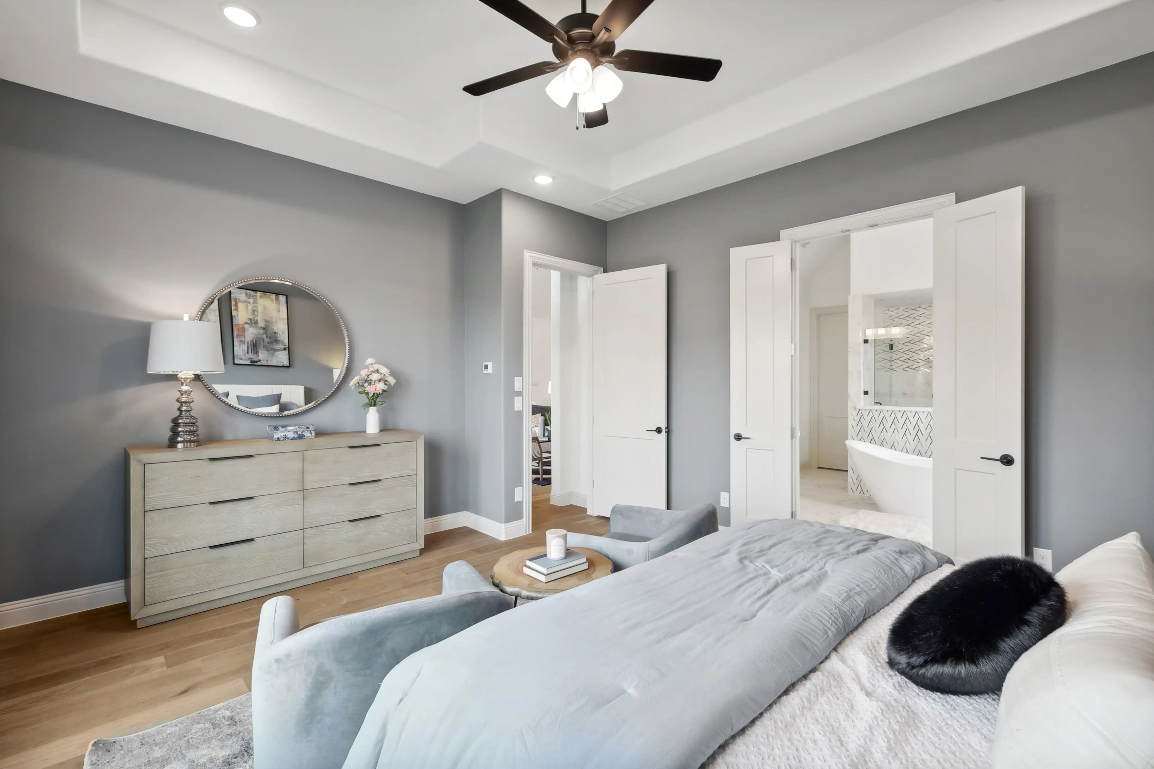 Modern Bedroom with En-Suite Bath in Westside Preserve Elegant bedroom with modern decor, featuring a round mirror, light wood dresser, and en-suite bath in Westside Preserve.