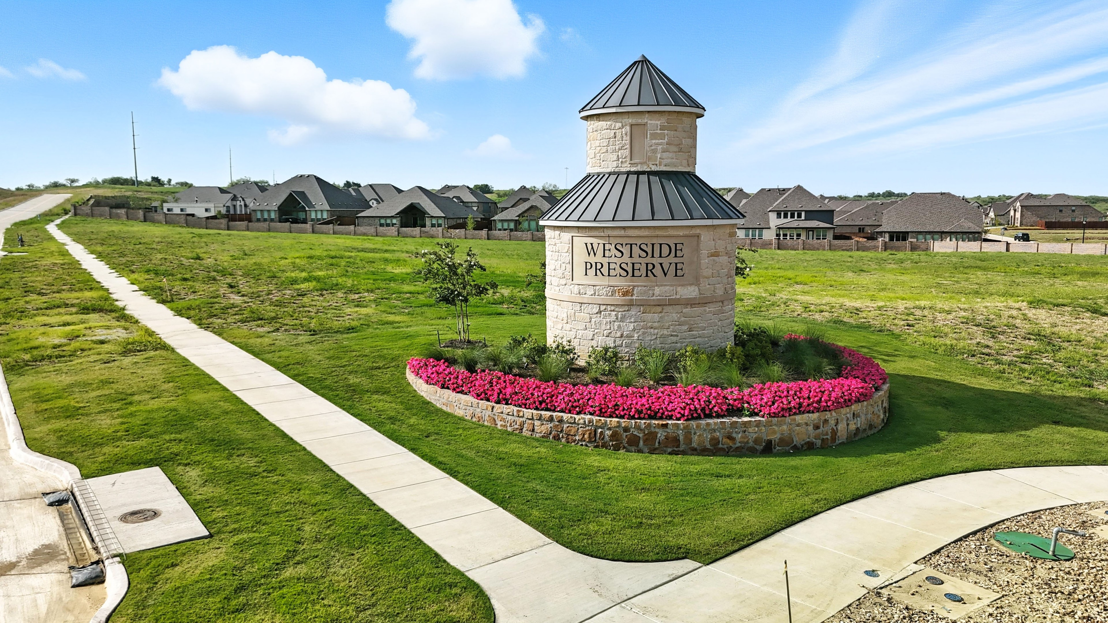 Westside Preserve Entrance with Stone Tower and Lush Landscaping Stone tower with "Westside Preserve" sign, surrounded by vibrant flowers, near modern homes in green landscape.