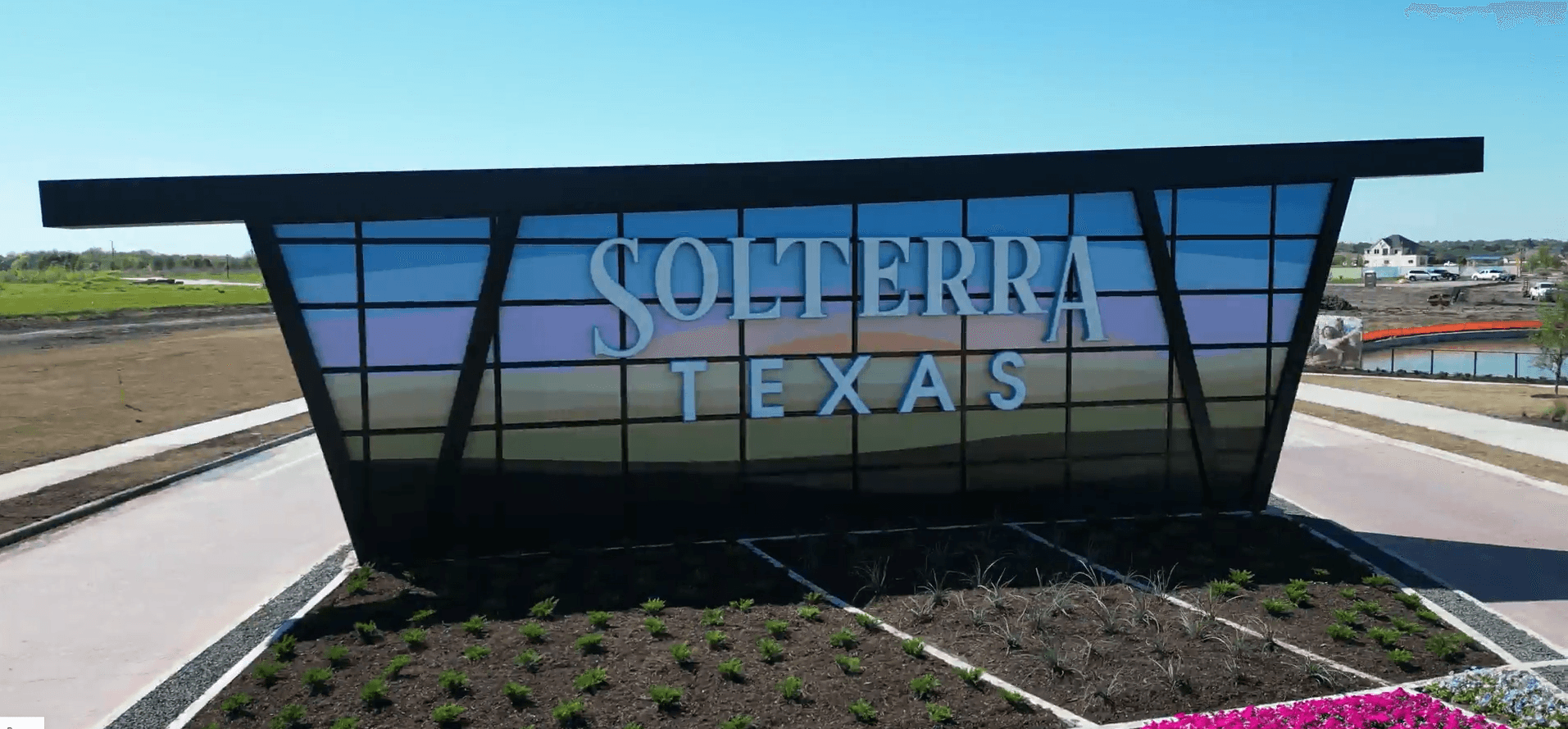 Solterra Texas Community Modern Glass Sign with Landscaping Modern glass sign for Solterra Texas community, angular design, lush landscaped garden, bright clear sky, serene surroundings.