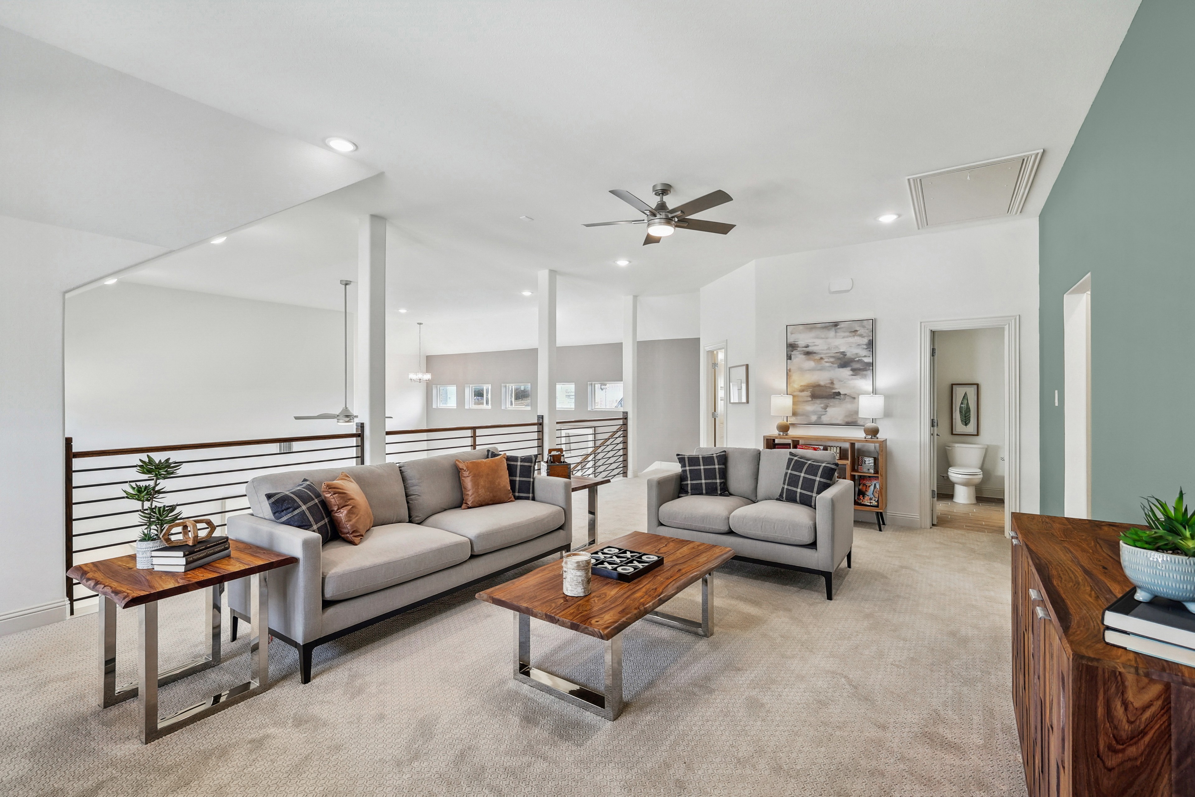 Elegant Solterra Texas Living Room Featuring Modern Design Elements Modern Texas lounge with plush sofas, wooden tables, ceiling fan, neutral tones, and railing. Located in Solterra community.