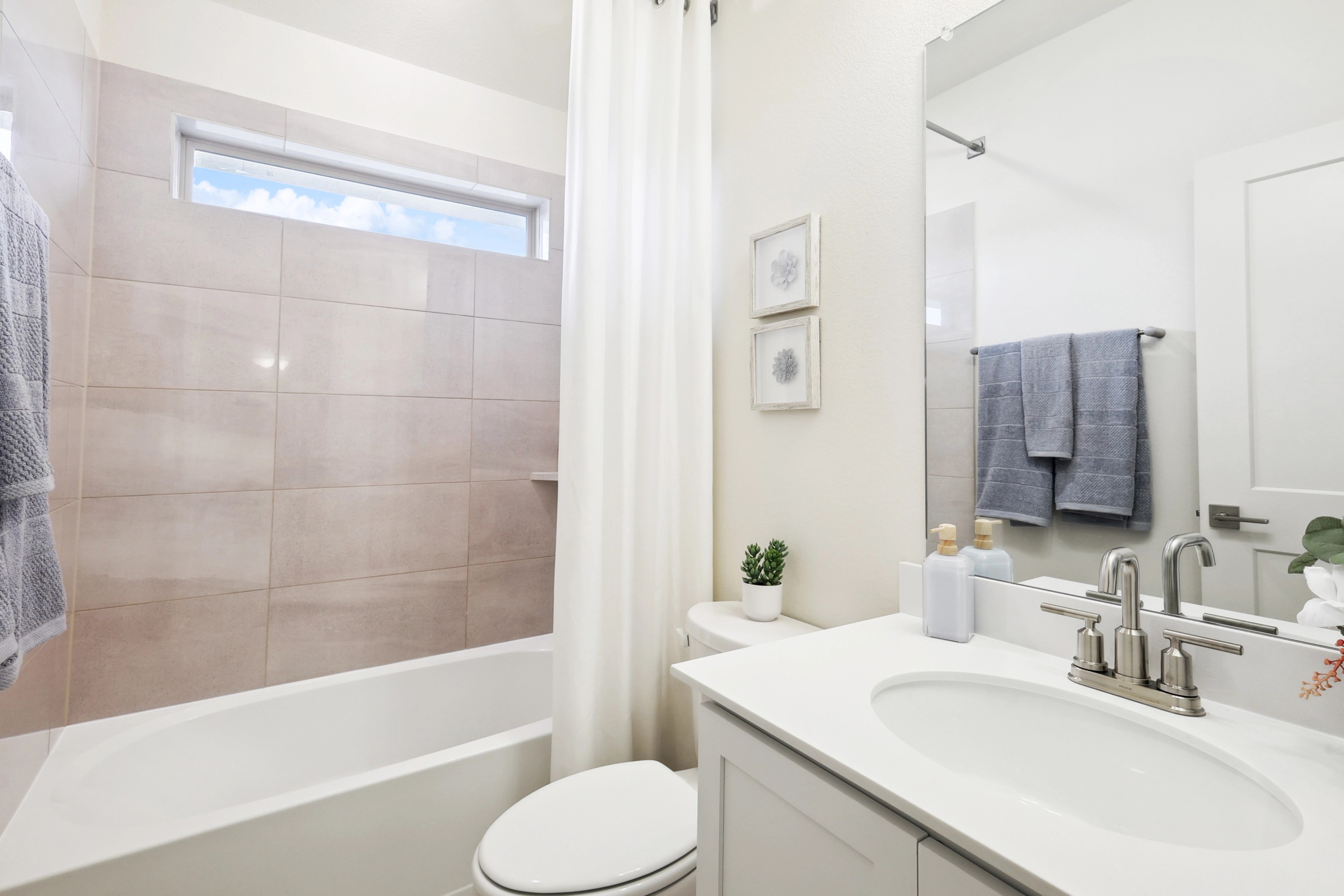 Modern Bathroom Design in The Oaks Community Modern bathroom with bathtub, beige tiles, minimalist decor, and window light in The Oaks community.