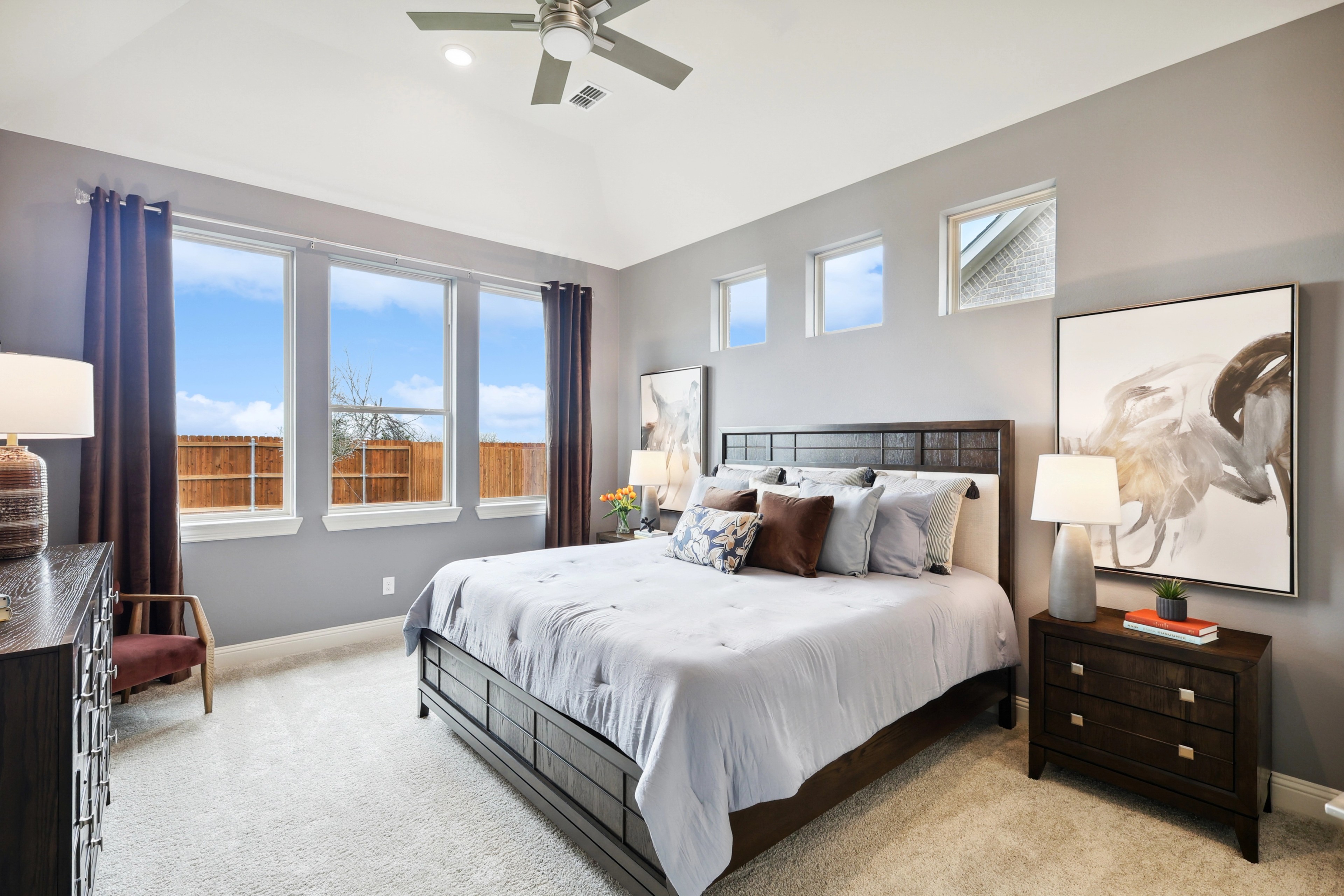 Luxurious Bedroom in The Oaks with Plush Carpeting and Large Windows Luxurious bedroom in The Oaks with plush carpeting, elegant decor, and large windows. Modern ceiling fan enhances comfort.