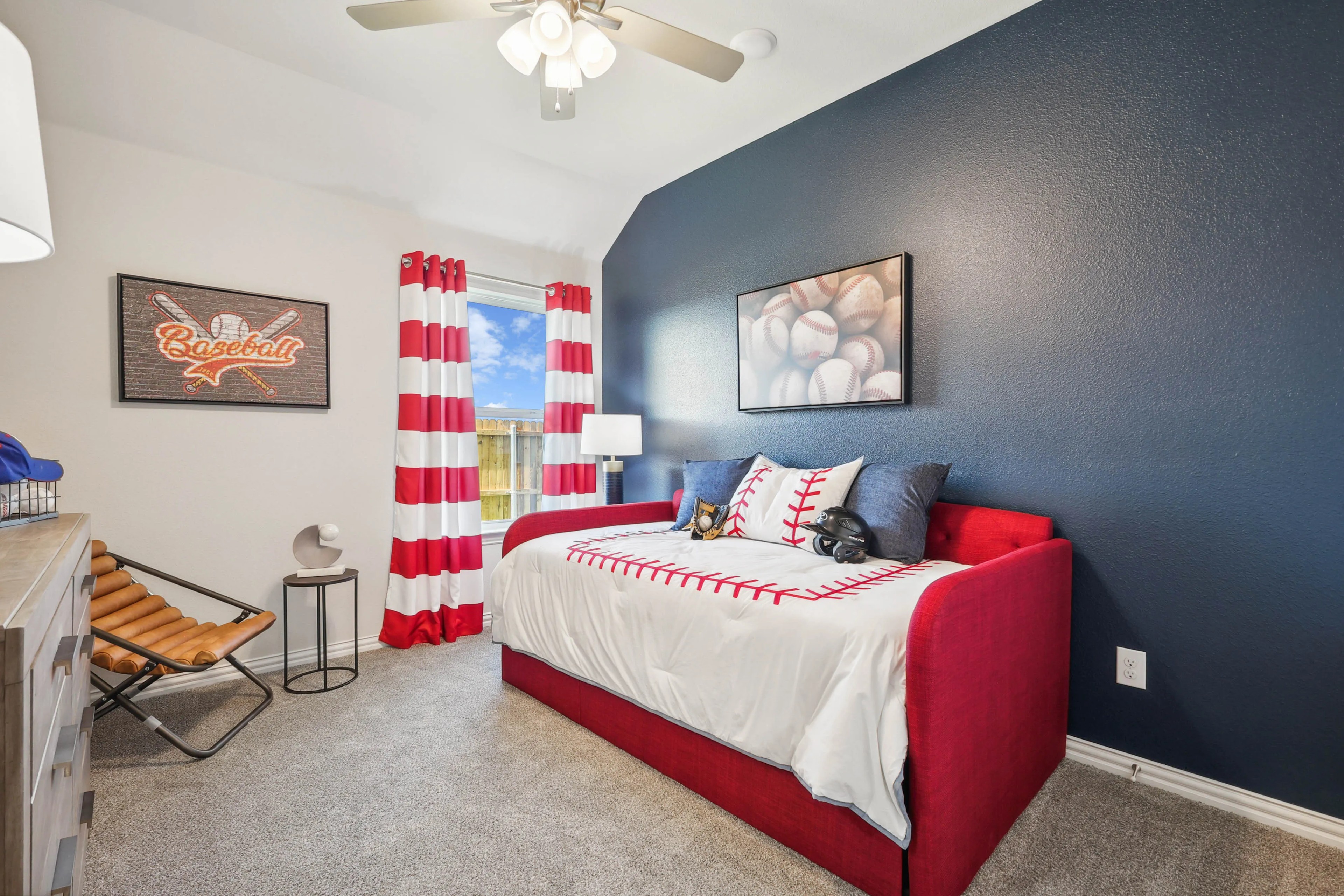 Baseball-Themed Bedroom in Pebblebrook Community Baseball-themed bedroom with a red daybed, striped curtains, and sports decor in Pebblebrook community.