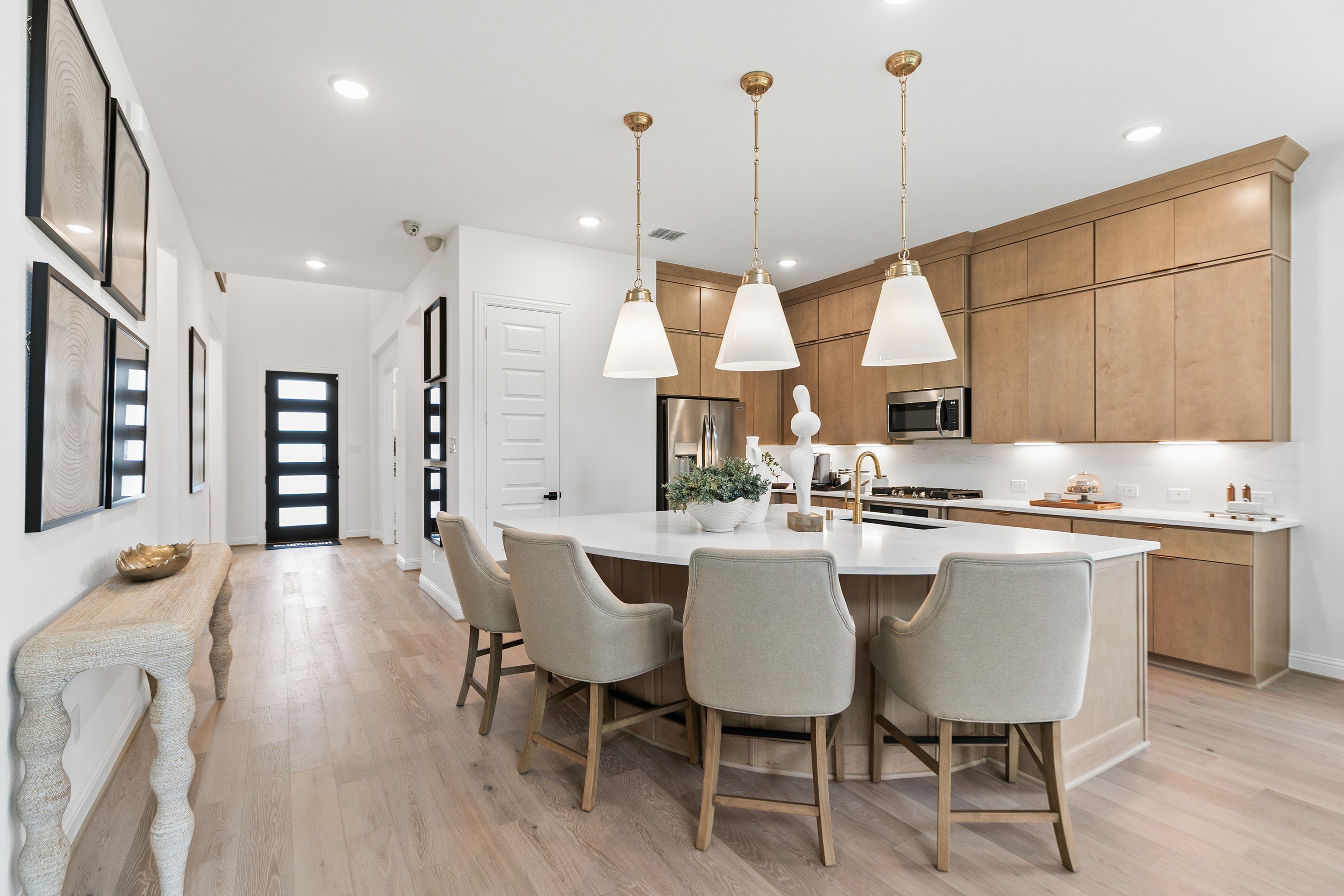 Modern Kitchen Design in Katy Lakes with Quartz Island Modern kitchen in Katy Lakes with quartz island, light wood cabinets, pendant lights, and beige chairs.