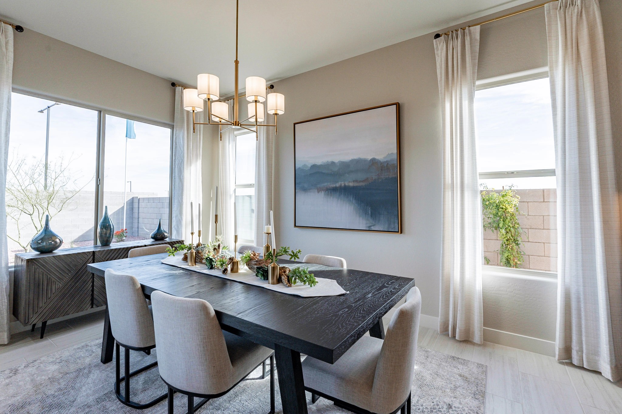 Luxurious Dining Room with Gold Chandelier in Arroyo Seco Elegant dining room with dark wood table, gold chandelier, large windows, and art in Arroyo Seco Hacienda community.
