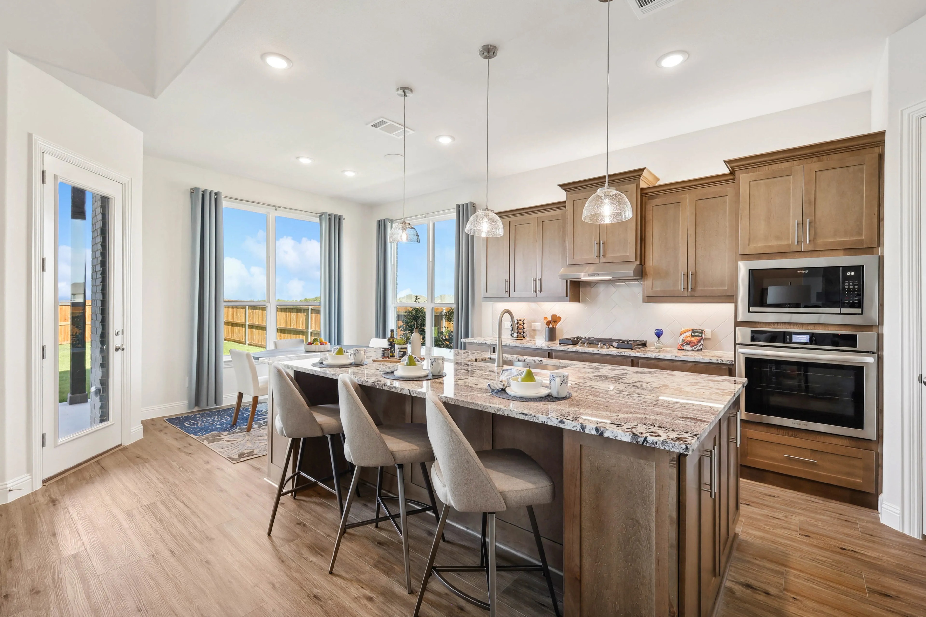 Ridge Crossing Modern Kitchen with Granite Island and Wood Cabinets Modern Ridge Crossing kitchen with granite island, wood cabinets, pendant lights, and large windows. Open airy design.