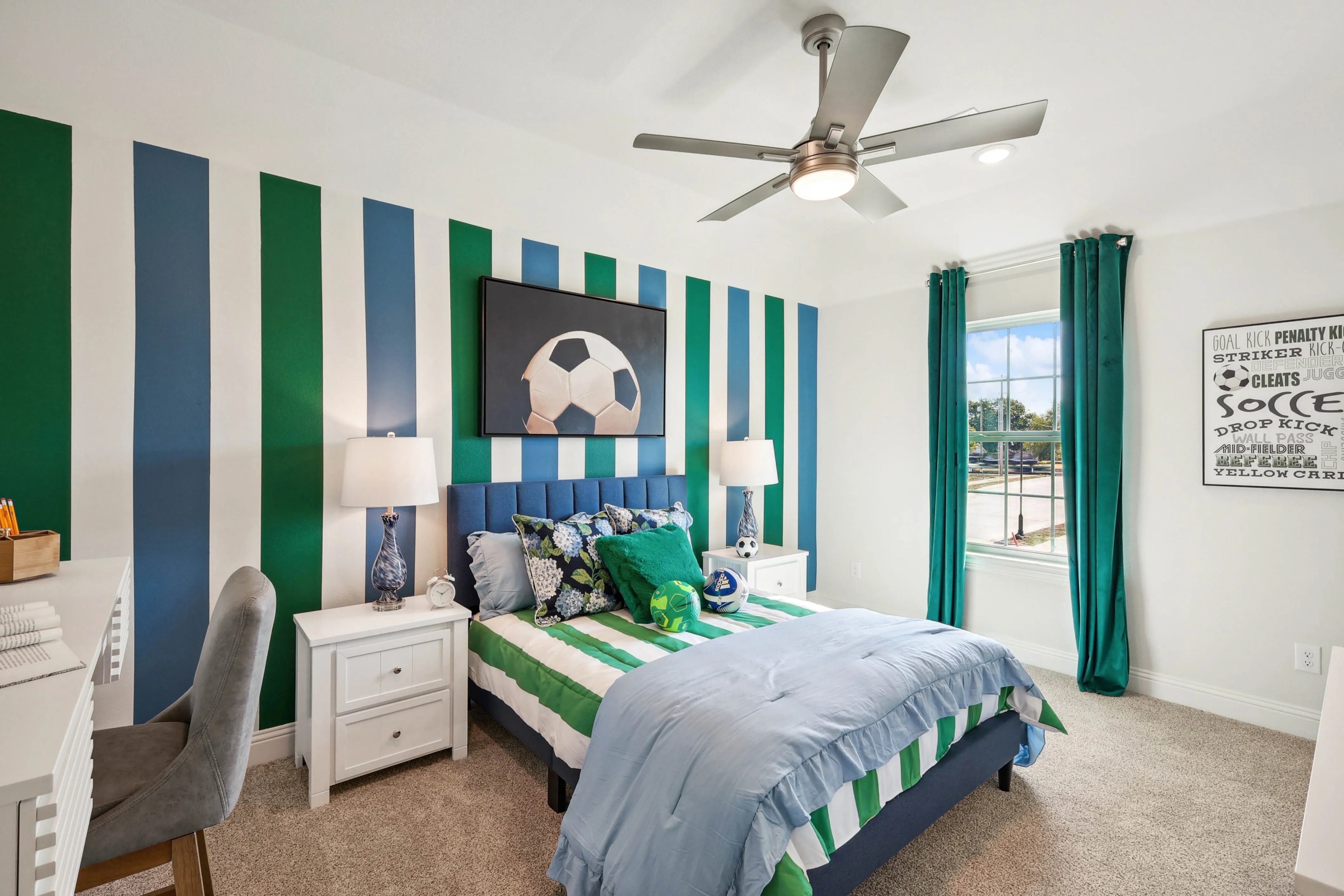 Soccer-Themed Bedroom at Ridge Crossing Community Modern bedroom with striped blue, green walls, soccer theme, at Ridge Crossing community. Large window, ceiling fan.