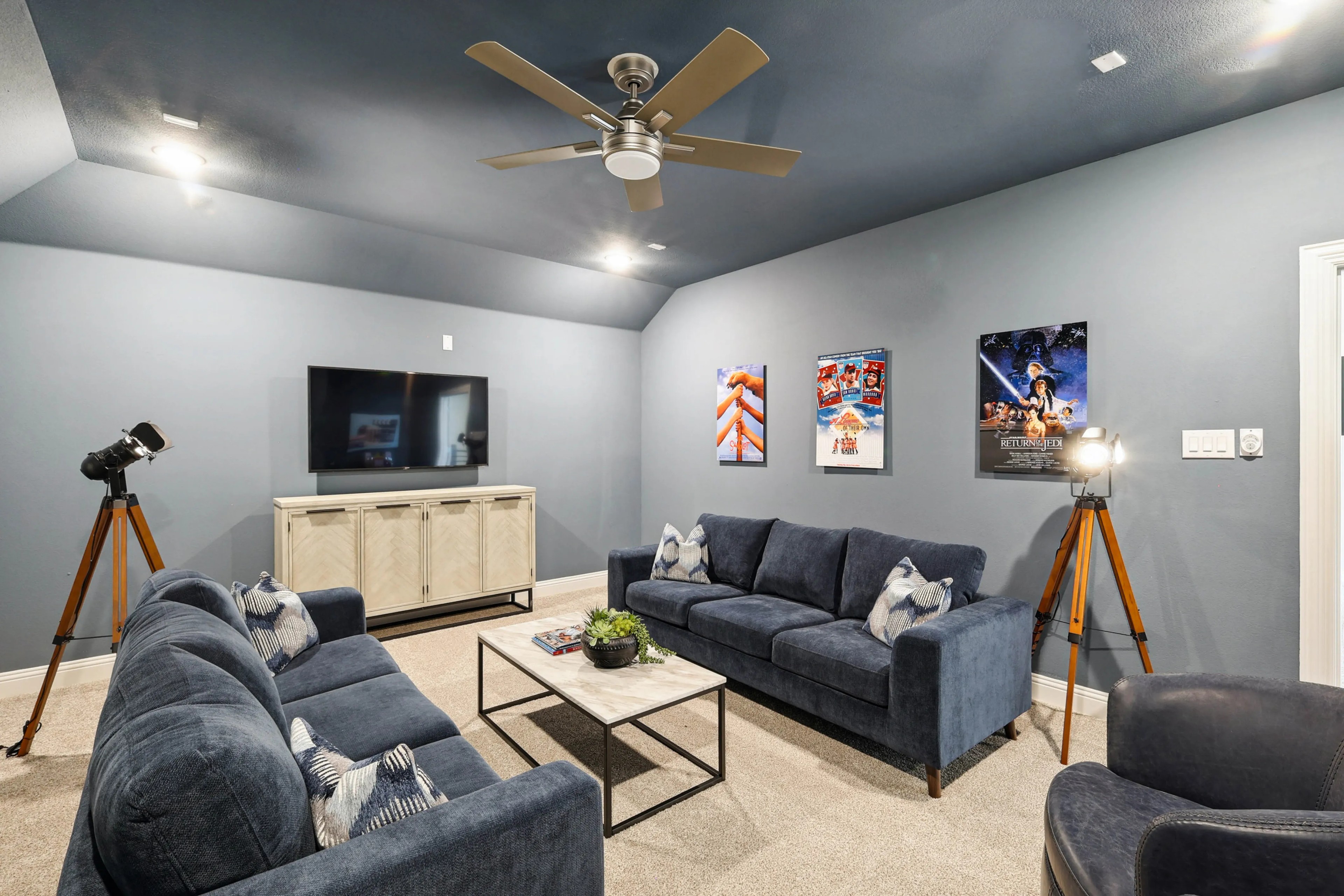 Luxurious Media Room in Ridge Crossing with Modern Decor Luxurious media room with plush navy sofas, modern lighting, and movie posters in Ridge Crossing community.