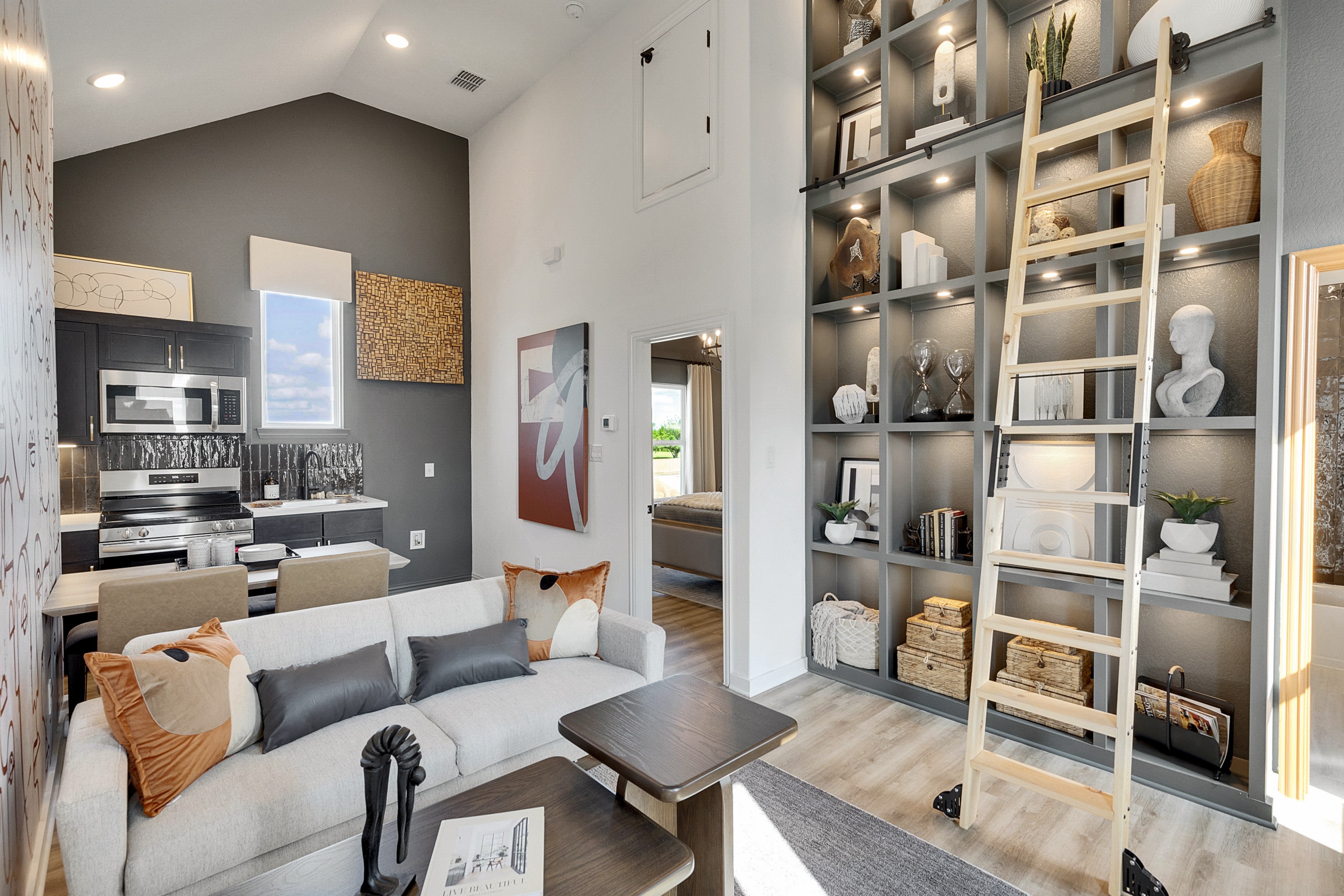 Modern Living Room with Custom Shelving in Spring Creek Modern living room in Spring Creek with high ceiling, custom shelving, and ladder. Open kitchen features sleek appliances.