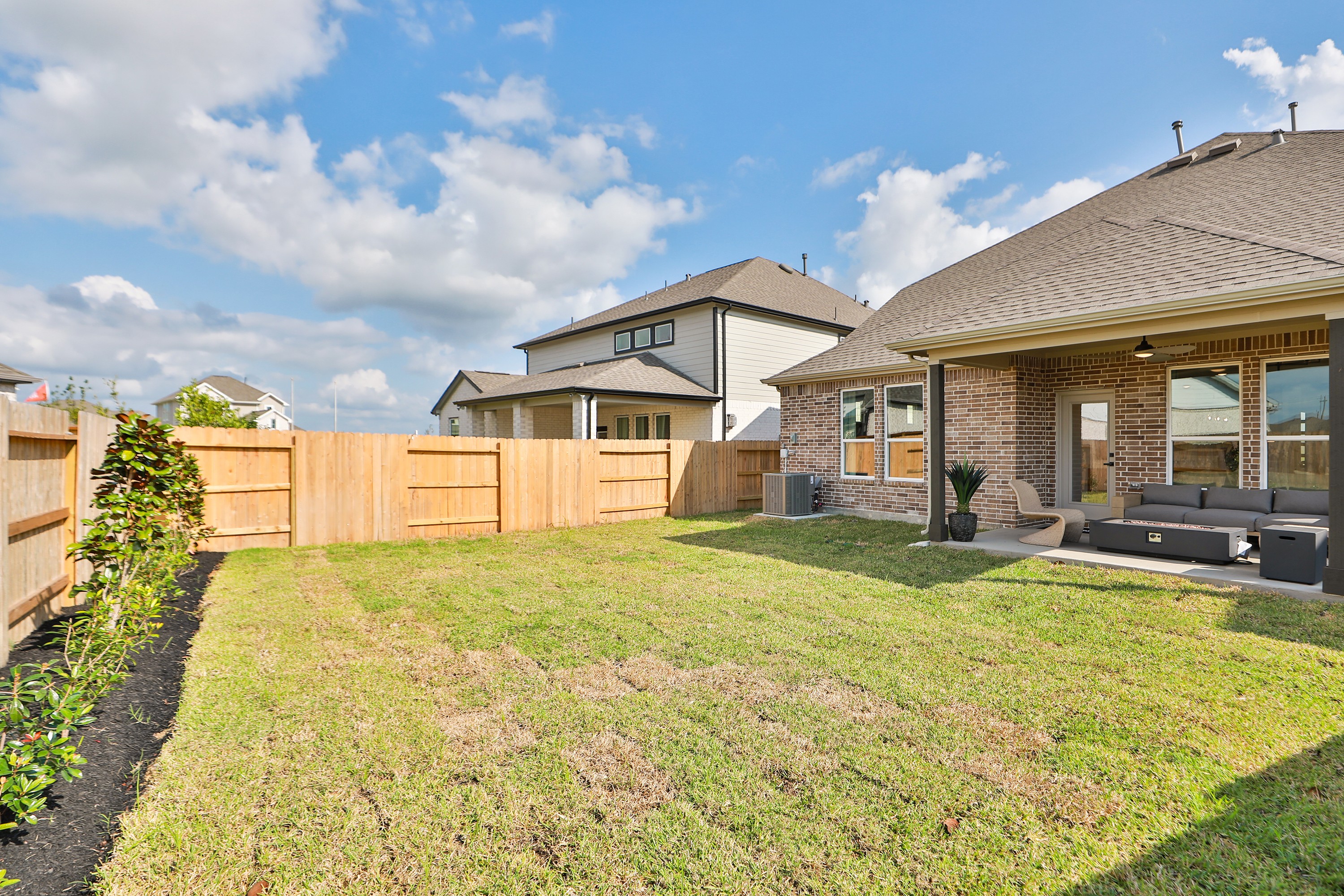 Backyard Patio with Wooden Fence and Seating, River Ranch Community Backyard with brick patio, wooden fence, and seating area in River Ranch community, featuring blue sky.