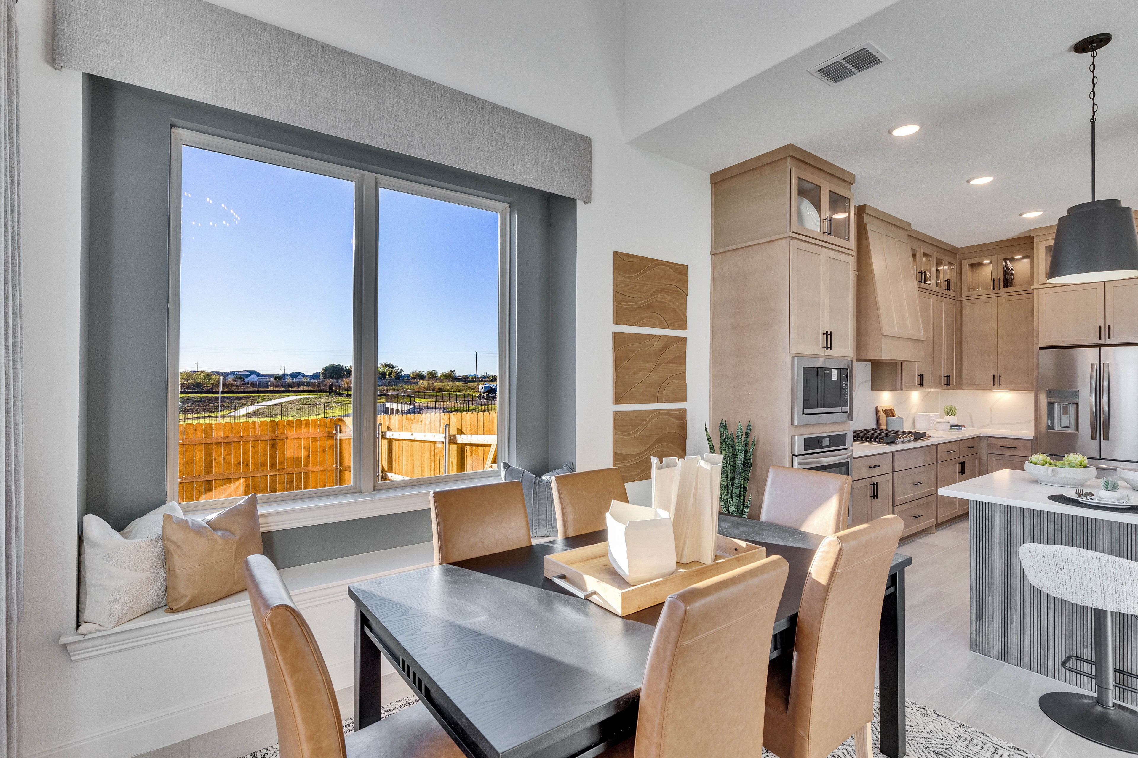 Modern Dining and Kitchen at Creeks Crossing Community Dining room with large window in Creeks Crossing, open kitchen with natural wood cabinets and modern decor.