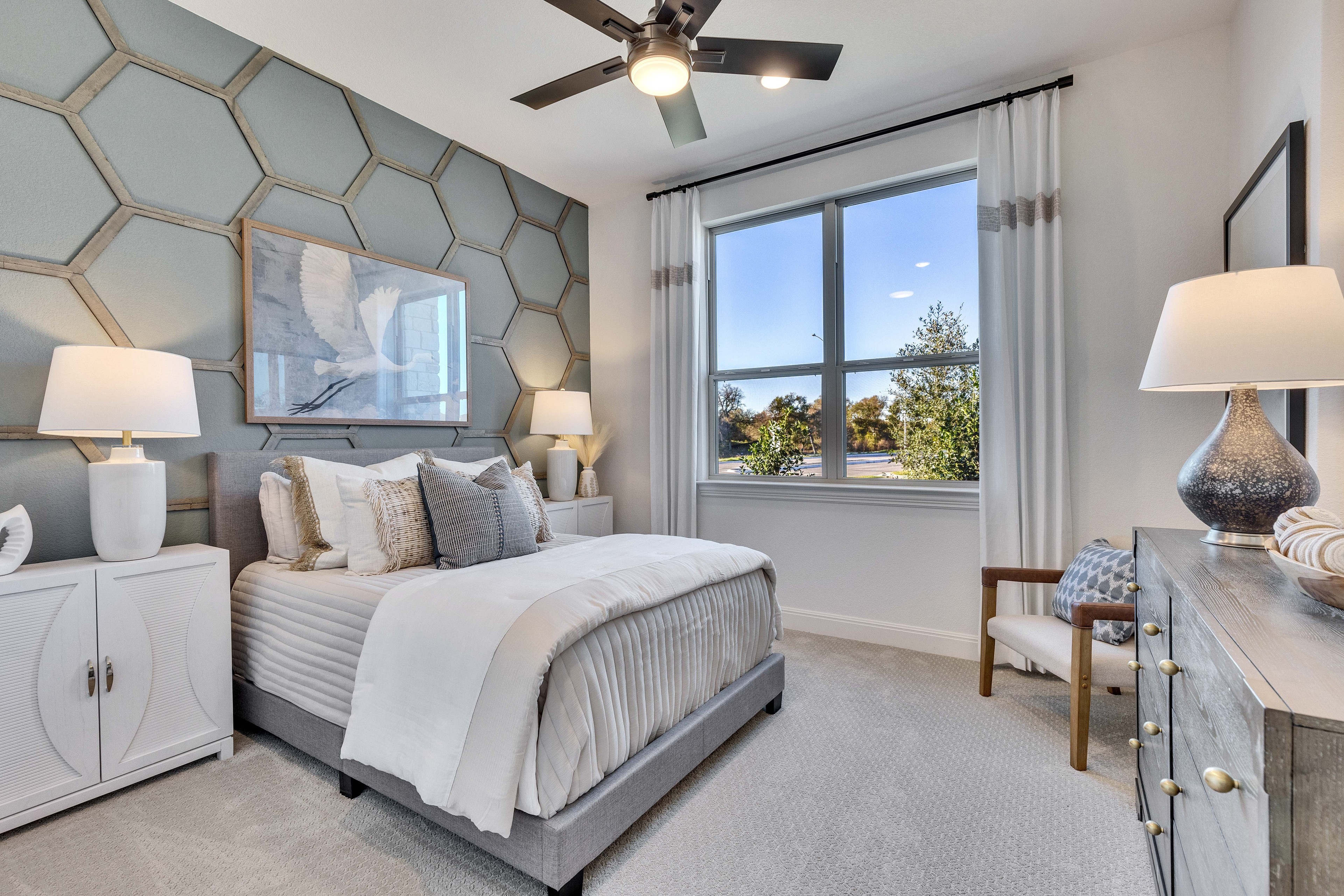Elegant Bedroom Design with Hexagonal Wall at Creeks Crossing Elegant bedroom with hexagonal accent wall, large window, modern furnishings in Creeks Crossing community.