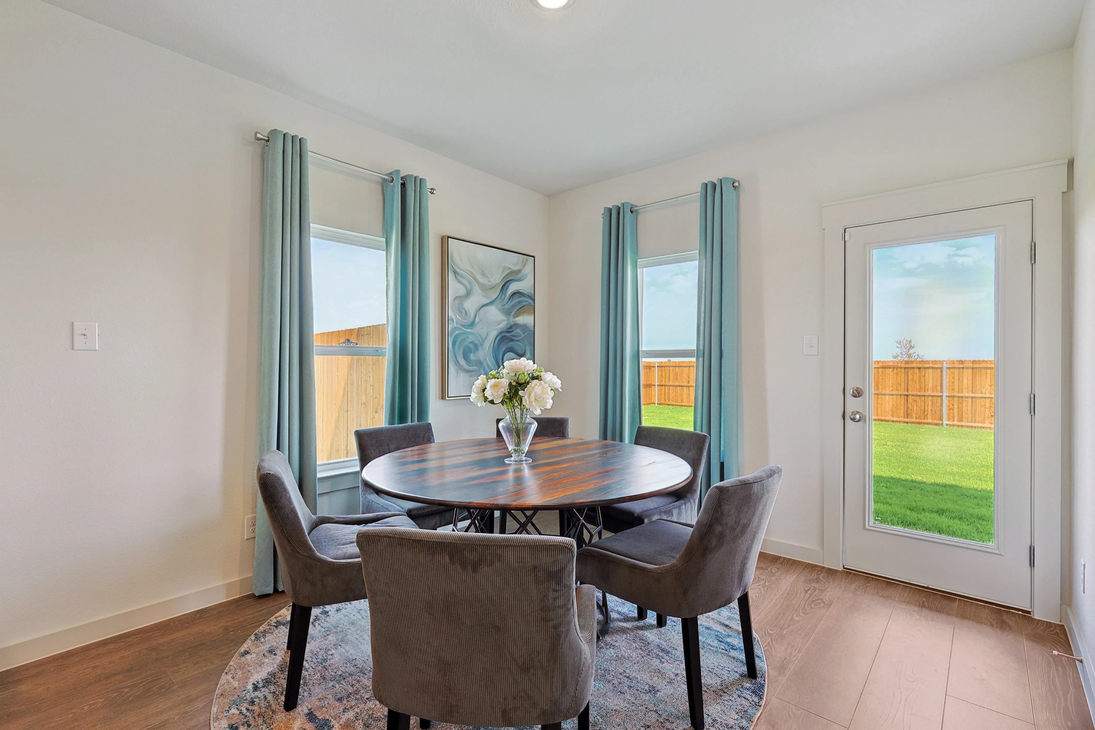 Stylish Dining Room with Round Table at Patriot Estates Elegant dining room with round wooden table, velvet chairs, large windows, artwork. Patriot Estates.