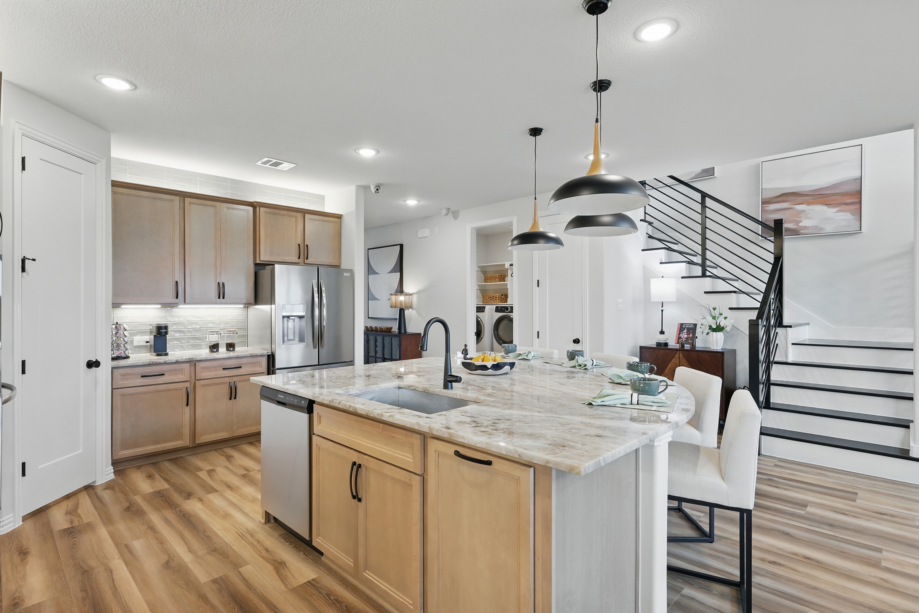 Modern Kitchen with Marble Island and Staircase in Westridge Modern kitchen in Westridge with marble island, pendant lights, and wood cabinets. Stylish staircase by dining area.
