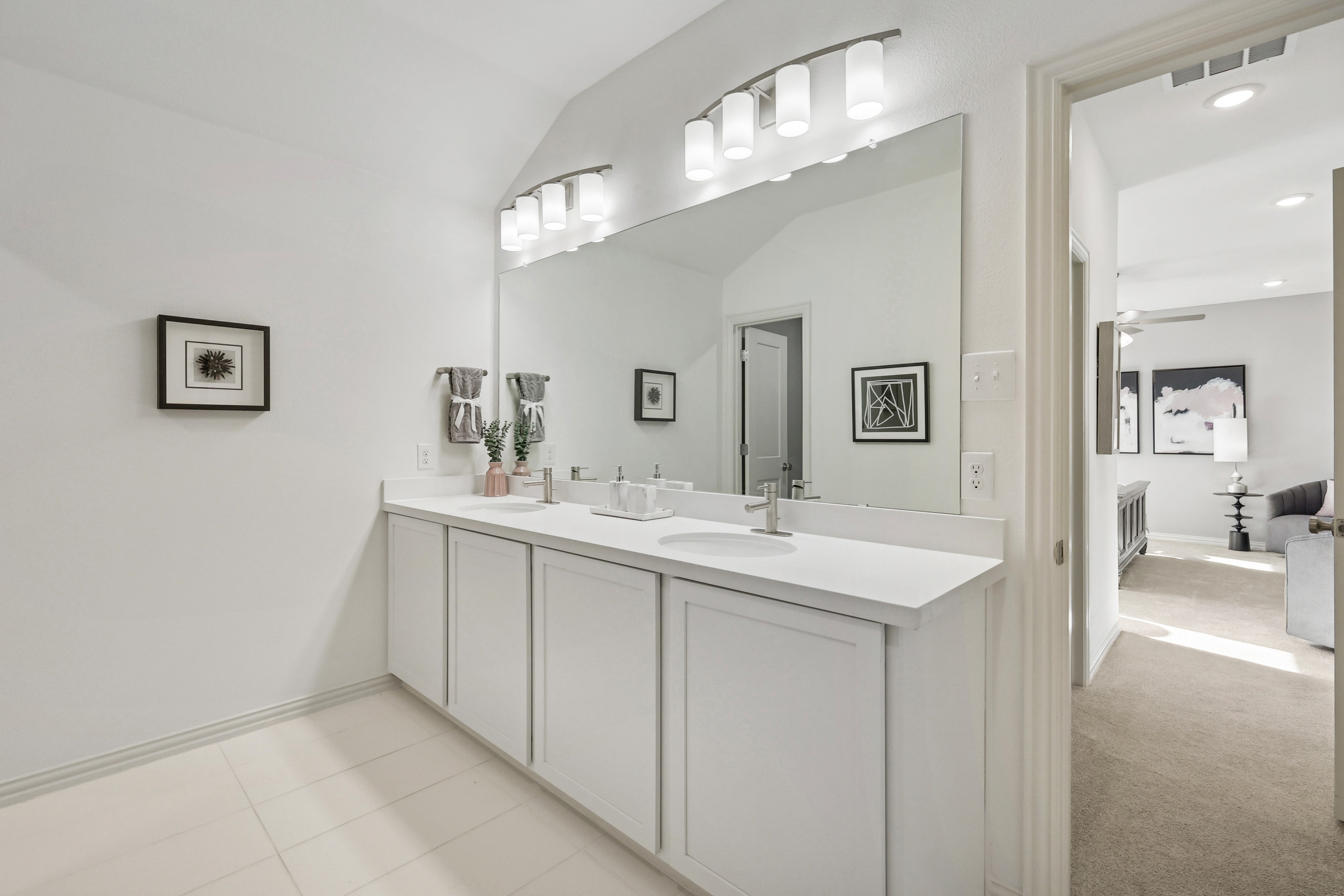 Modern Dual Vanity Bathroom in Bel Air Village Home Elegant white bathroom with dual sinks and large mirror in Bel Air Village. Modern lighting, framed art on walls.