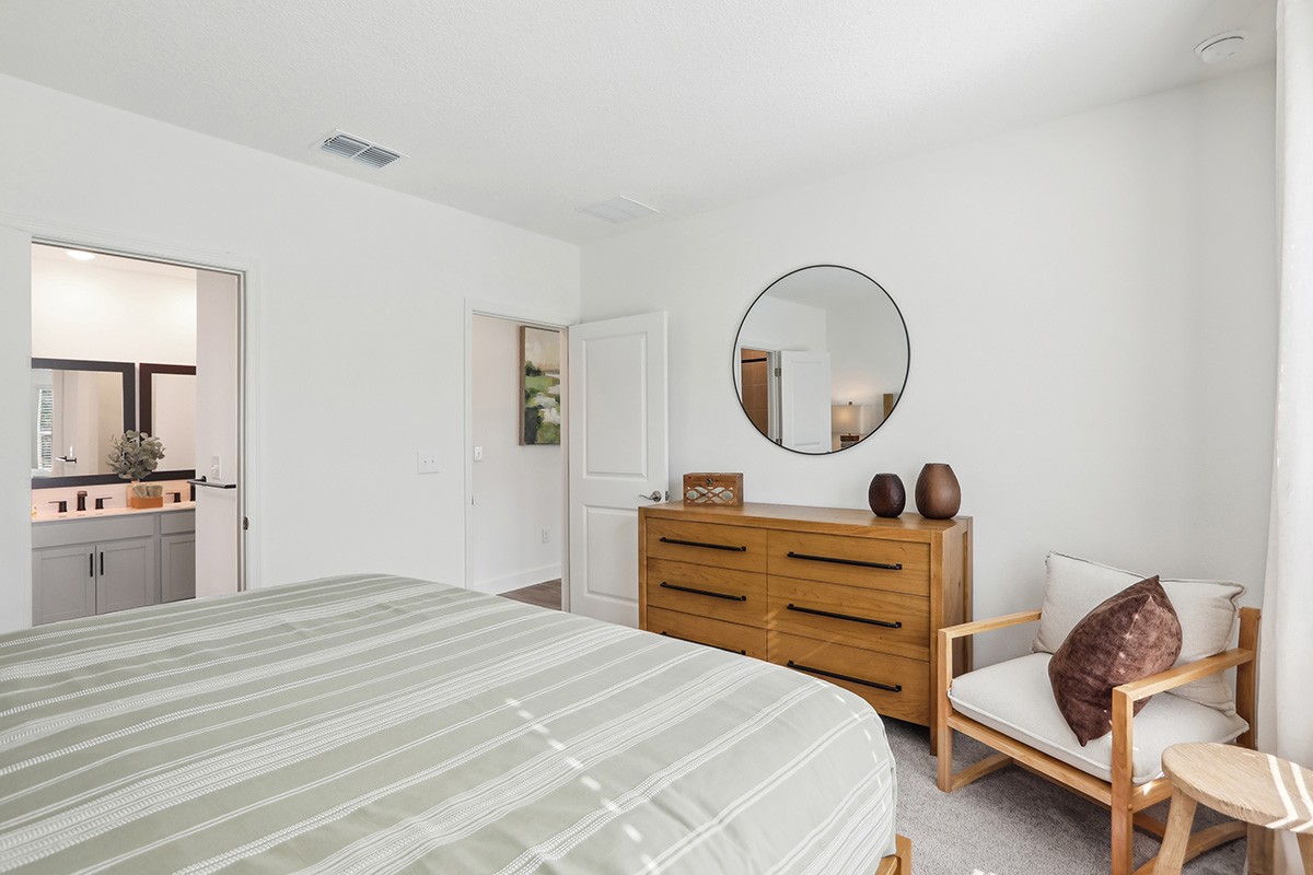Spring Hill Bedroom with Modern Design and En-Suite Bathroom Modern Spring Hill bedroom with wood dresser, round mirror, and en-suite bathroom.