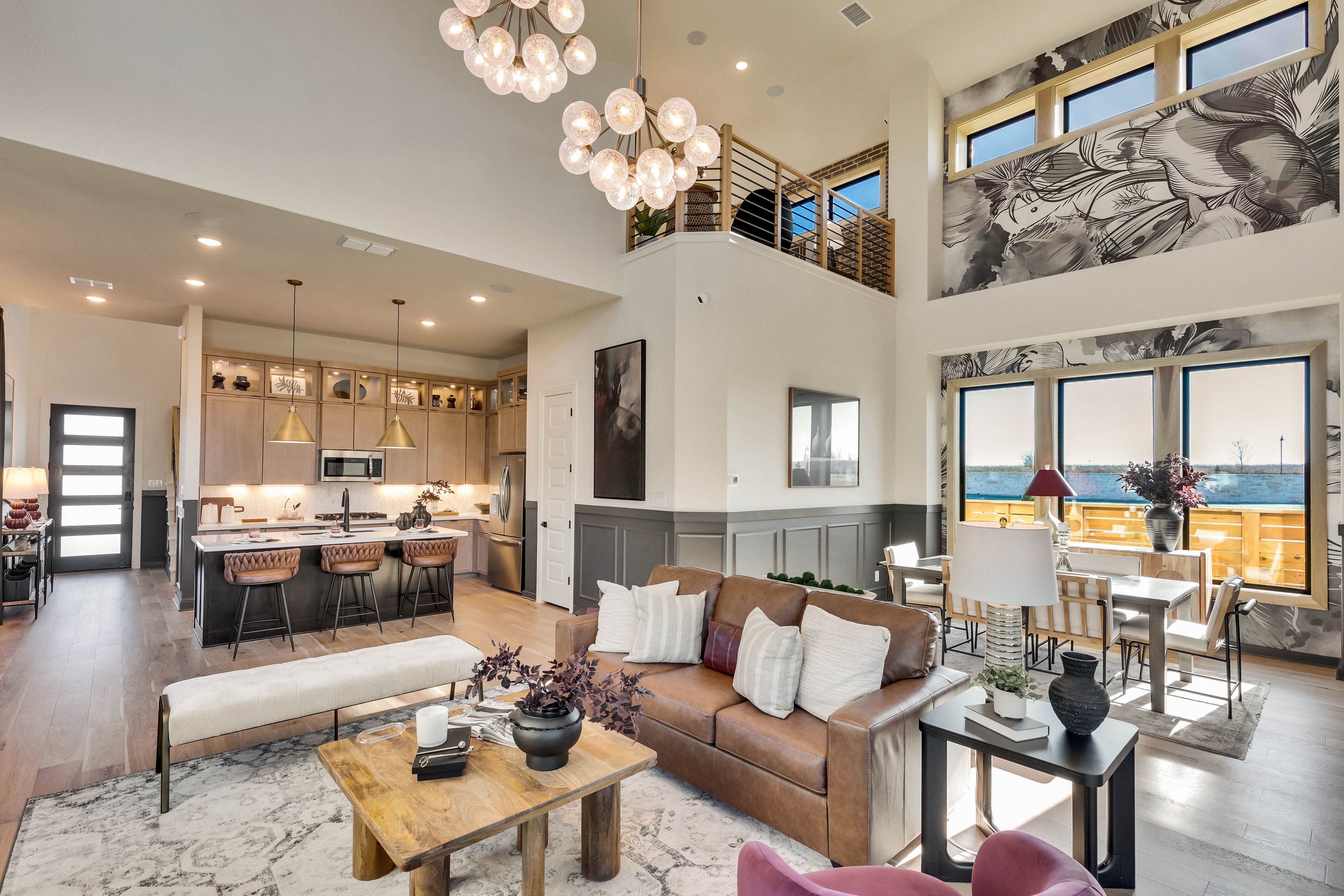 Elegant Open Living Area with High Ceilings in Flora Community Luxurious open-concept living room and kitchen with high ceilings, chandelier, and floral wallpaper in Flora community.