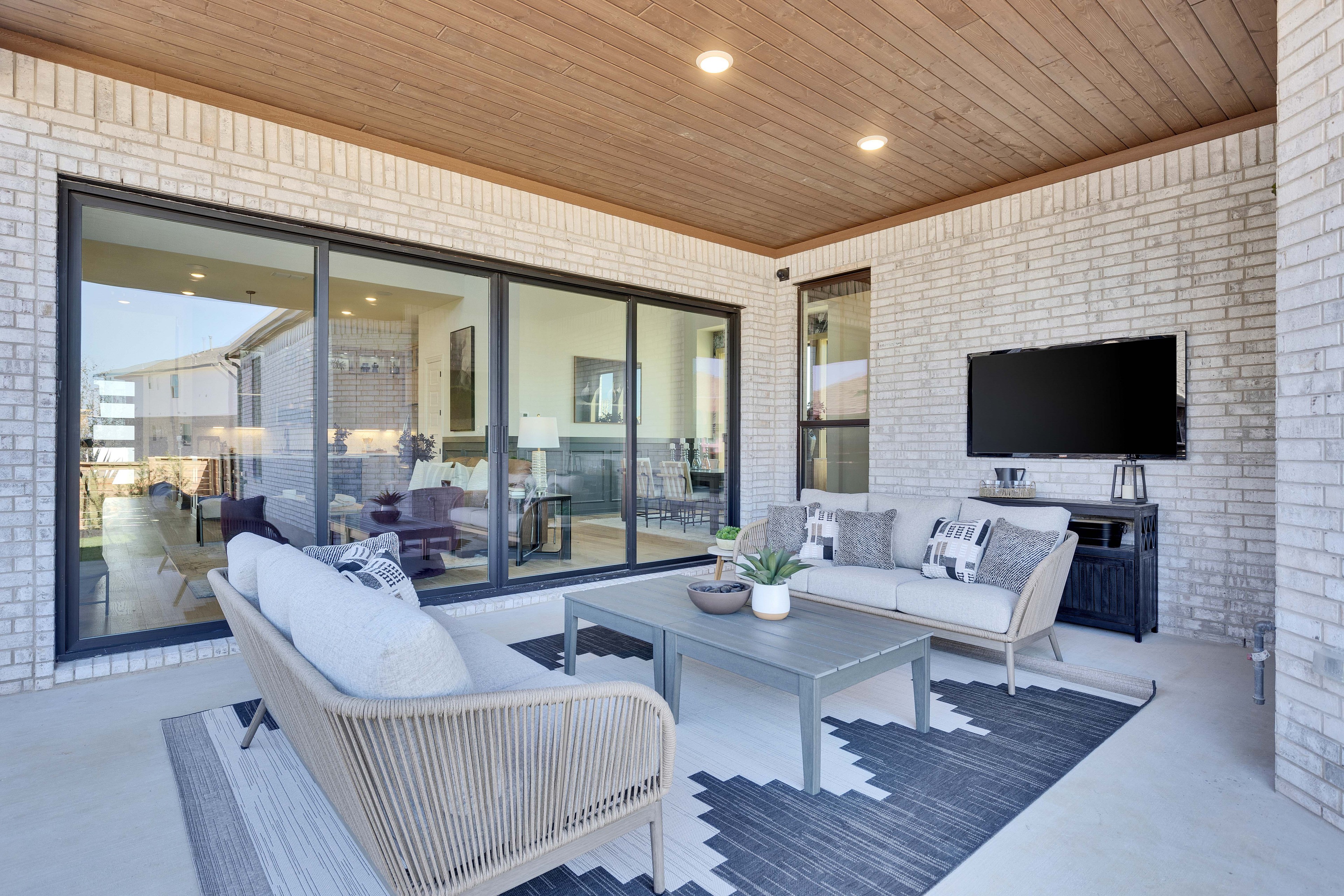 Stylish Patio with Elegant Décor in Flora Community. Modern patio with cushioned seating, large glass doors, white brick walls, Flora community.