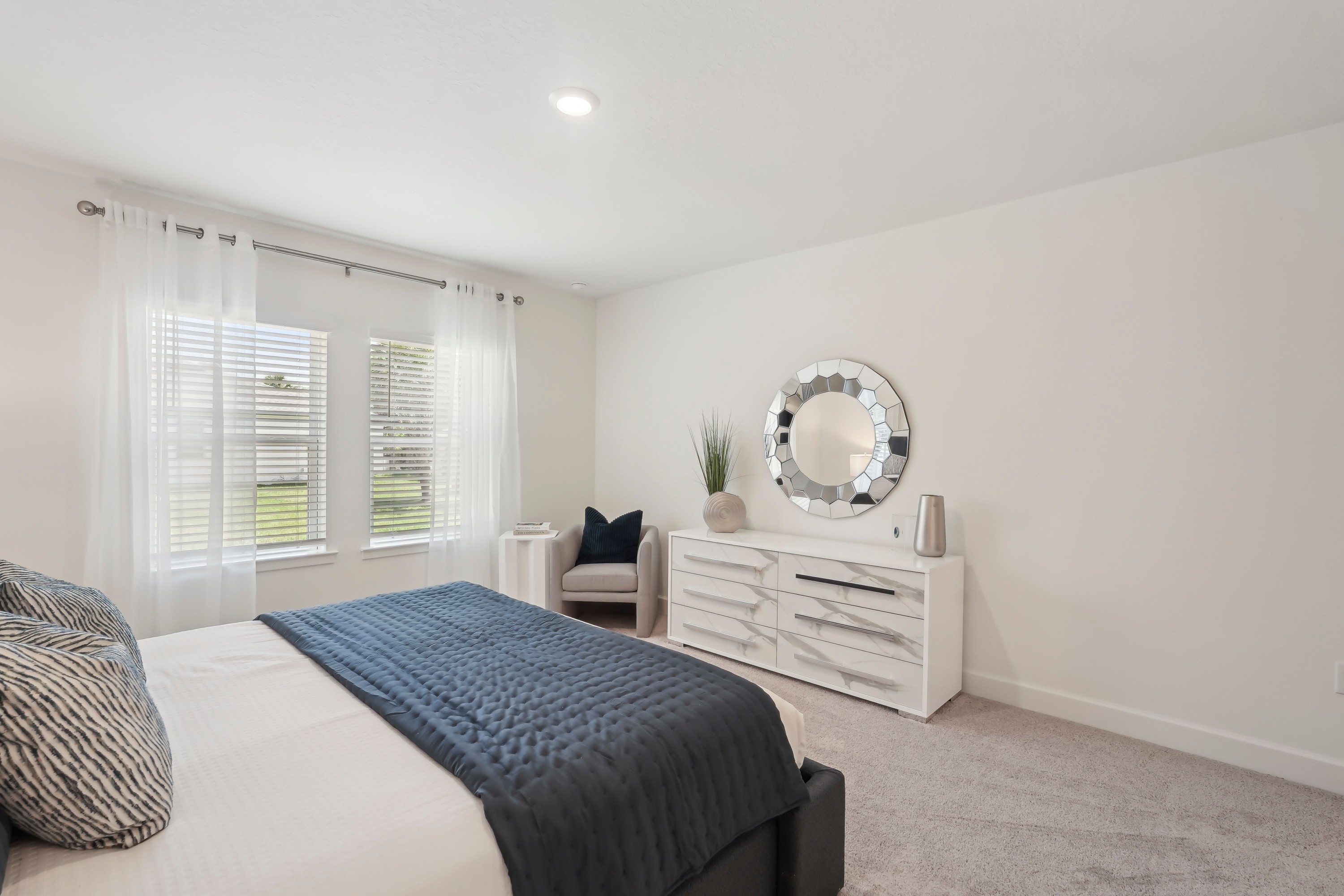 Modern Bedroom Design in North Port Home Bright North Port bedroom with white dresser, round mirror, and large windows.