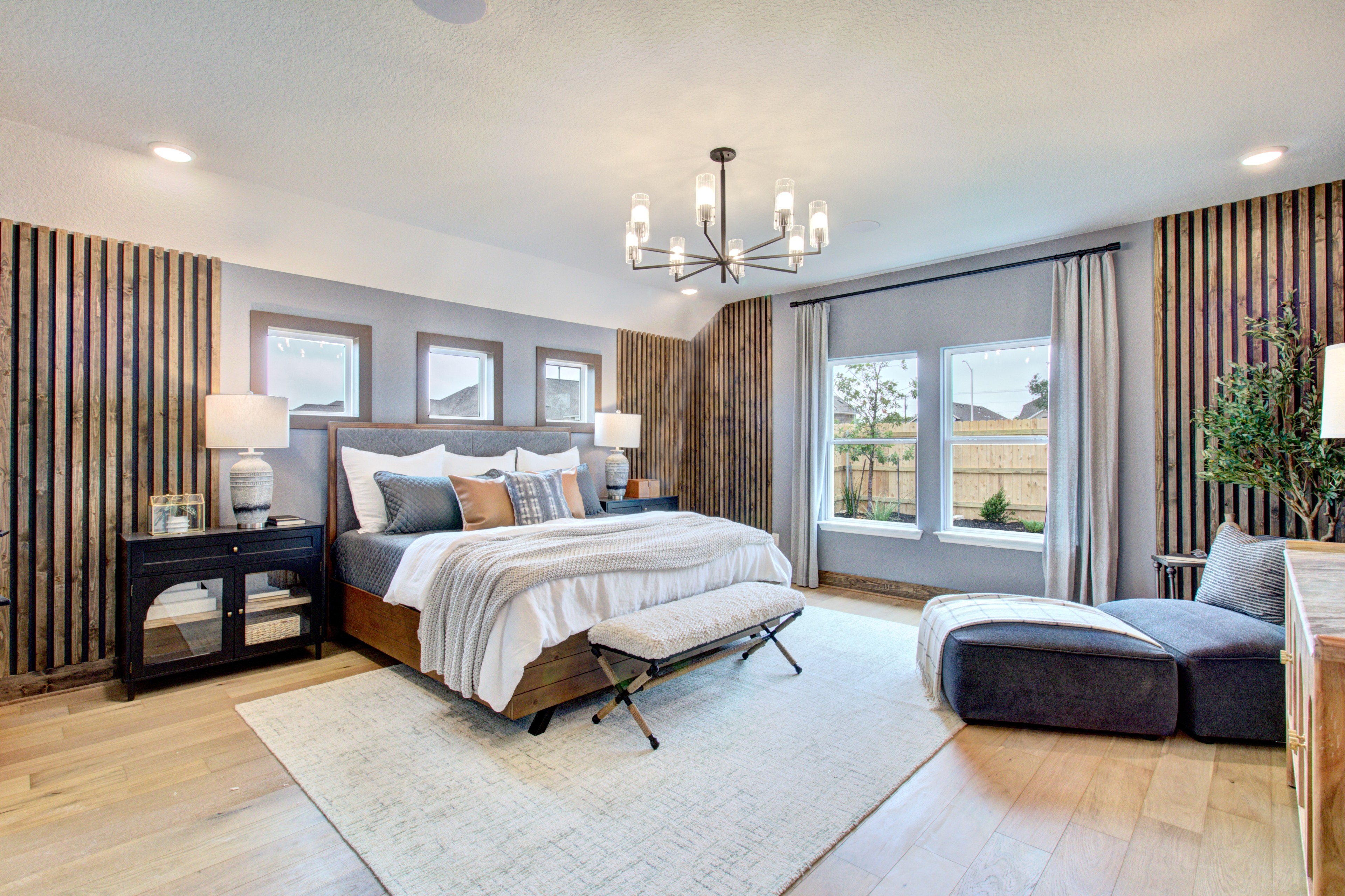 Luxurious Bedroom with Wood Accents in Sunflower Ridge Elegant bedroom with modern chandelier, wood accents, and large windows in Sunflower Ridge community.