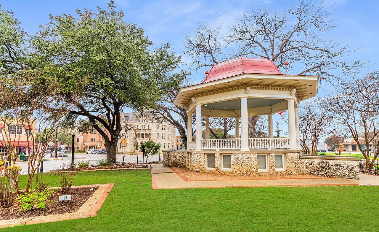 Gazebo with Red Roof in Quaint Town Square Park Setting Gazebo with red roof in lush park setting, surrounded by trees in a quaint town square location. Architectural detail noted.