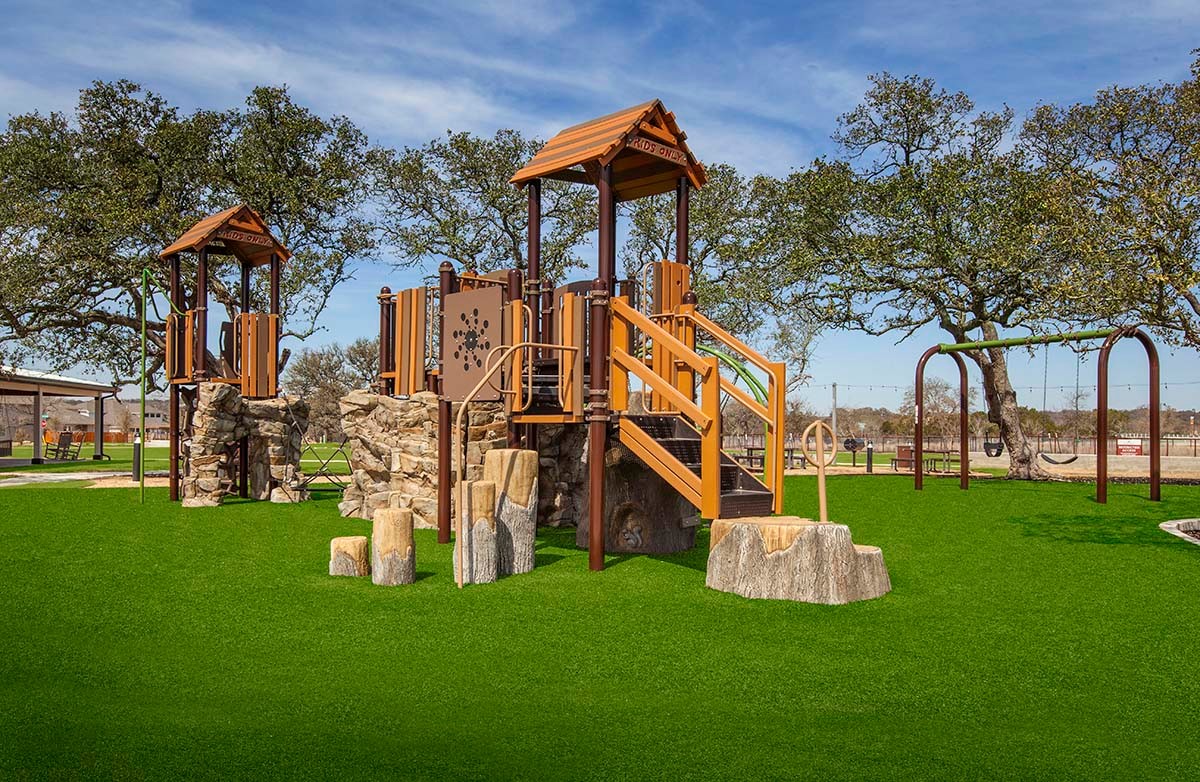 Meyer Ranch Playground with Wooden Structures in Enclave Community Modern playground with wooden elements at Meyer Ranch, set amidst lush green lawns and mature trees.