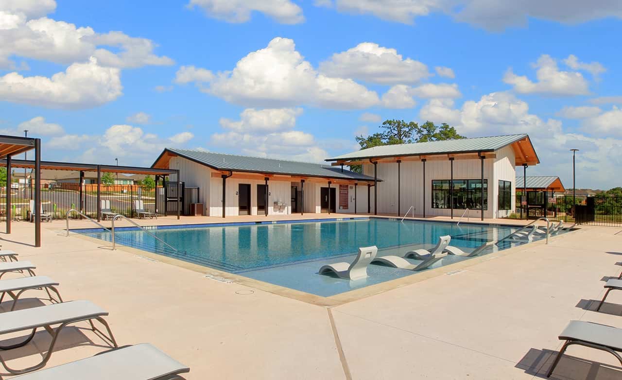 Meyer Ranch Texas - Modern Pool and Clubhouse Architecture Modern pool with lounge chairs, barn-style clubhouse, Meyer Ranch, Texas, clear sky, luxurious amenities.