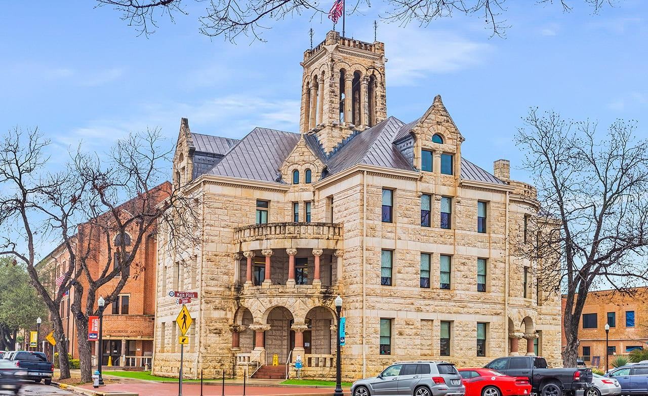 Historic Seguin Texas Stone Courthouse with Tower and Arches Historic stone courthouse with ornate tower in Seguin, Texas, featuring arches and columns. Urban setting with parked cars.
