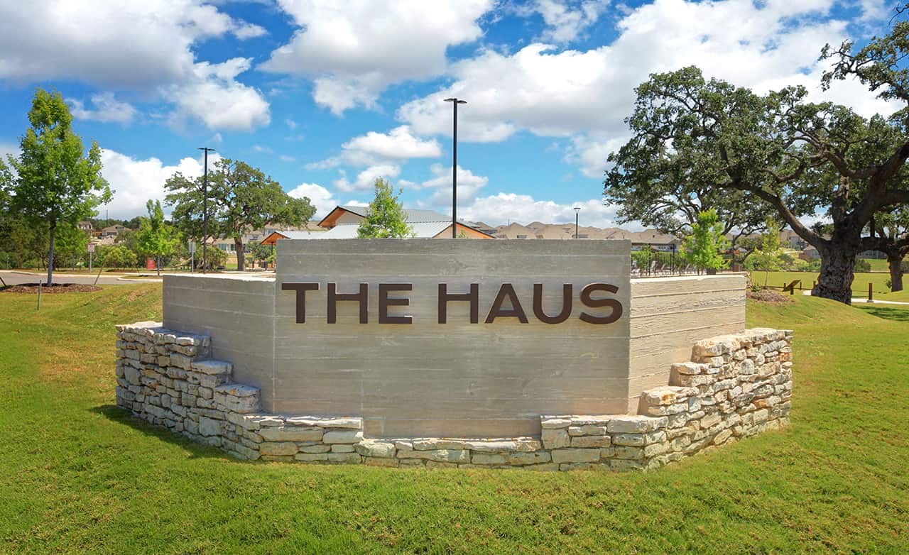 "Entrance Sign 'The Haus' at Meyer Ranch Community" "Stone and concrete sign reading 'The Haus' at Meyer Ranch, surrounded by trees under a bright sky."