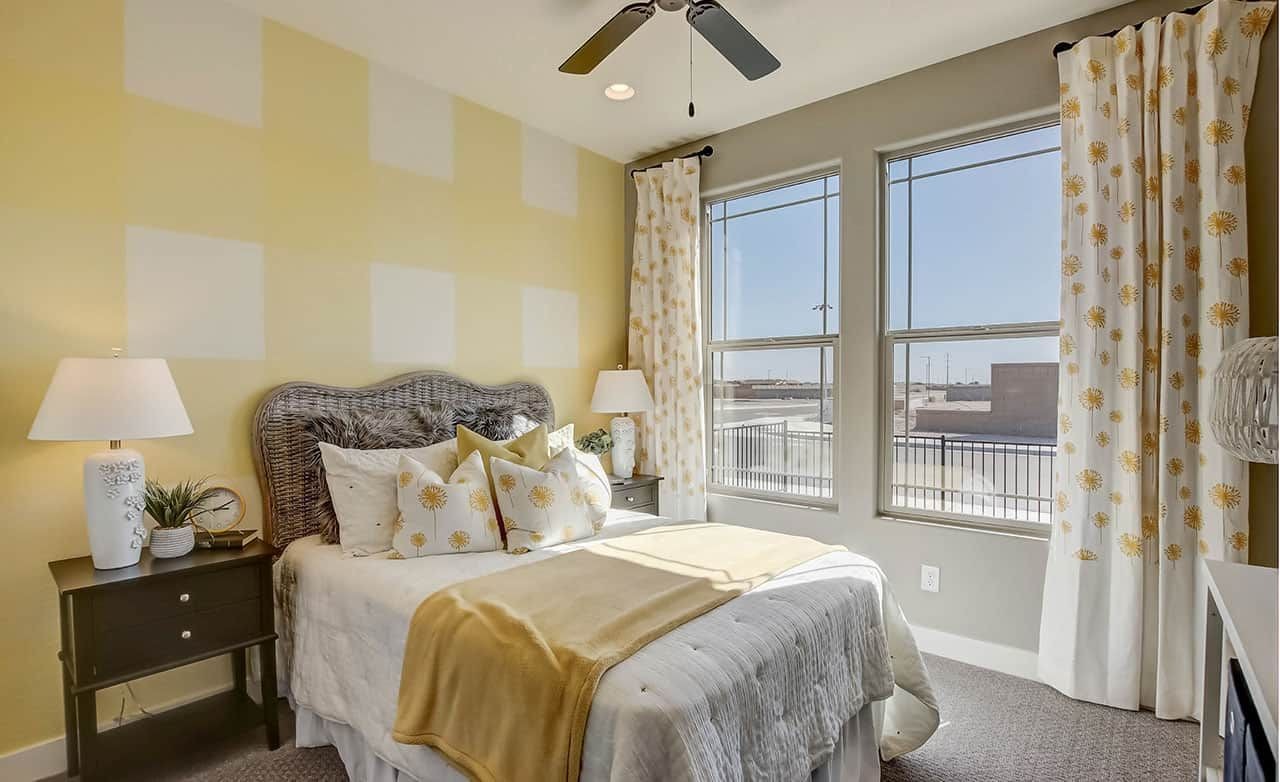 Elegant Bedroom with Wicker Headboard at Castillo, Anderson Parc Cozy bedroom with wicker headboard, yellow accents, large windows, floral curtains at Castillo at Anderson Parc.