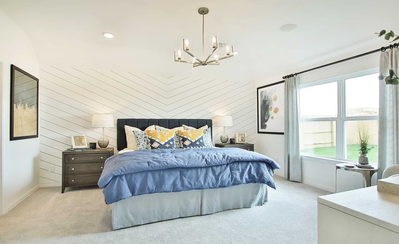 Chevron Accent Bedroom with Modern Chandelier in Oakwood Estates Elegant bedroom with chevron accent wall, blue bedding, modern chandelier, large window in Oakwood Estates.